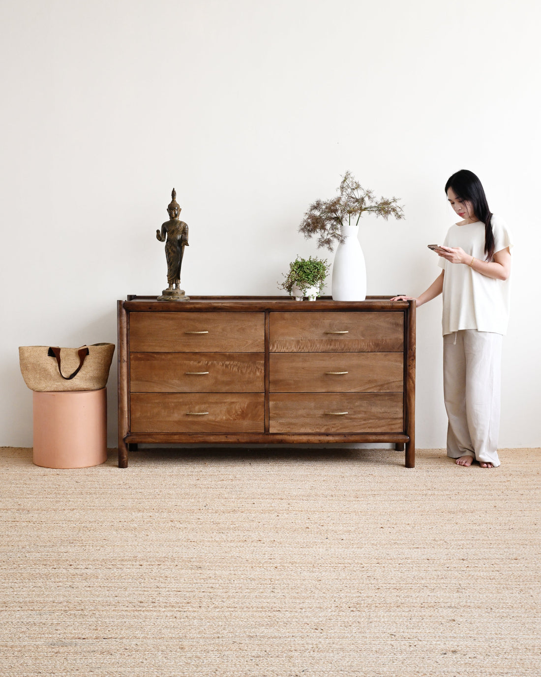 Woman standing next to a wooden dresser in a minimalistic room.