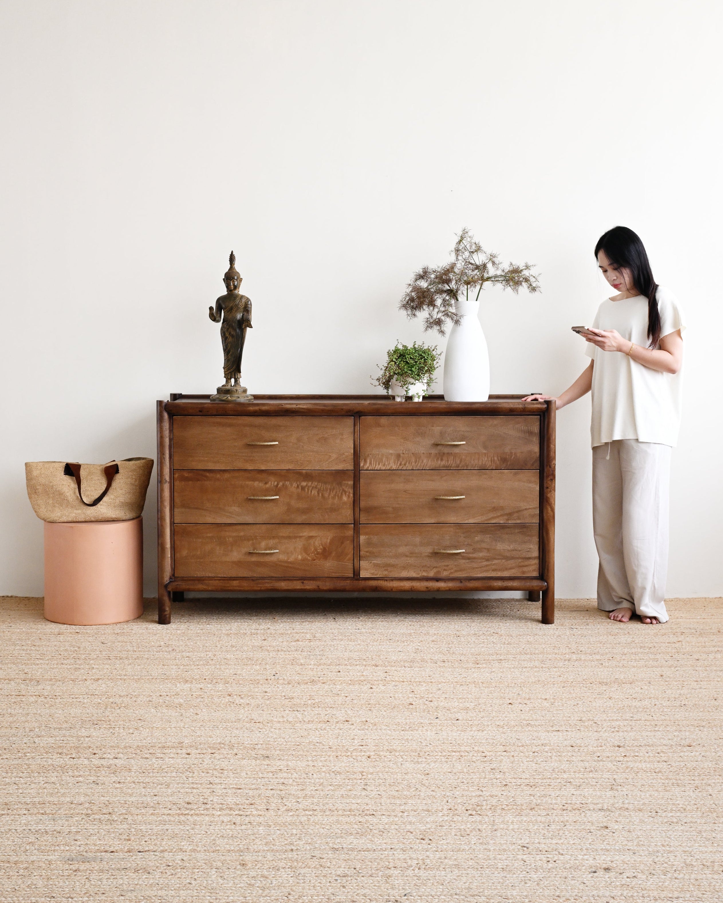 Woman standing next to a wooden dresser in a minimalistic room.