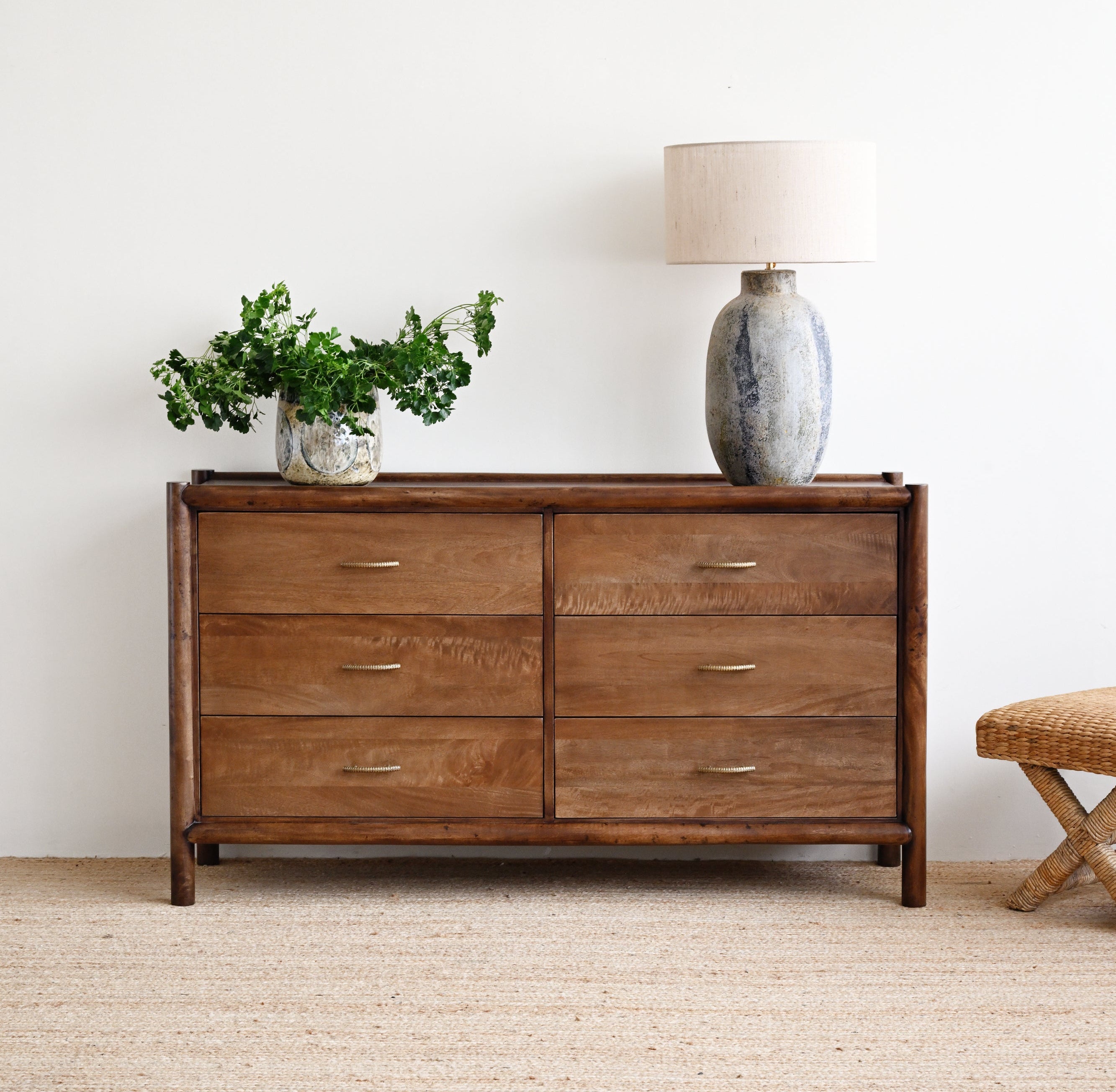 Wooden dresser with decorative items in a room with a white wall and beige carpet.