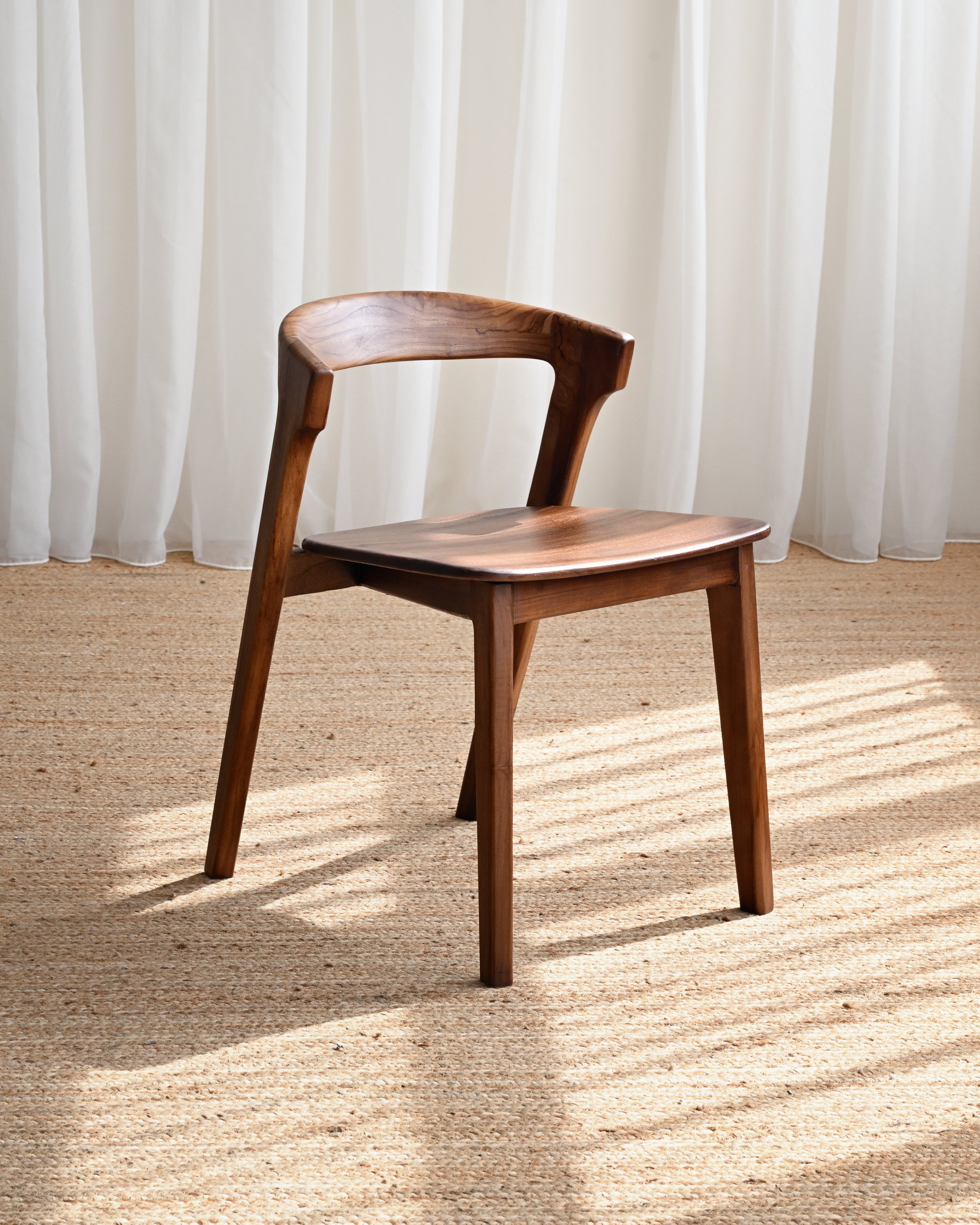 Wooden chair on a textured floor with white curtains in the background