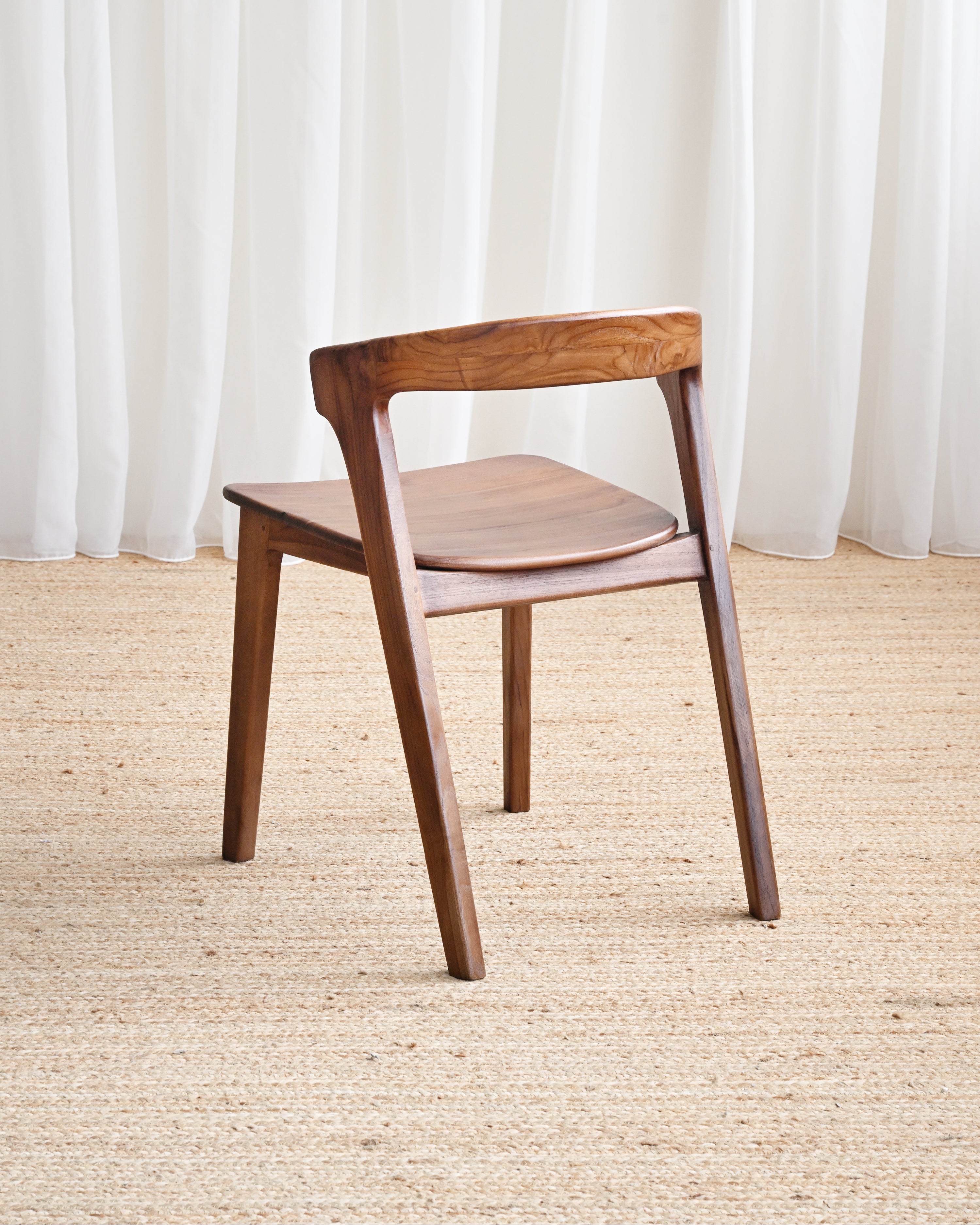 Wooden chair on a beige carpet with white curtains in the background