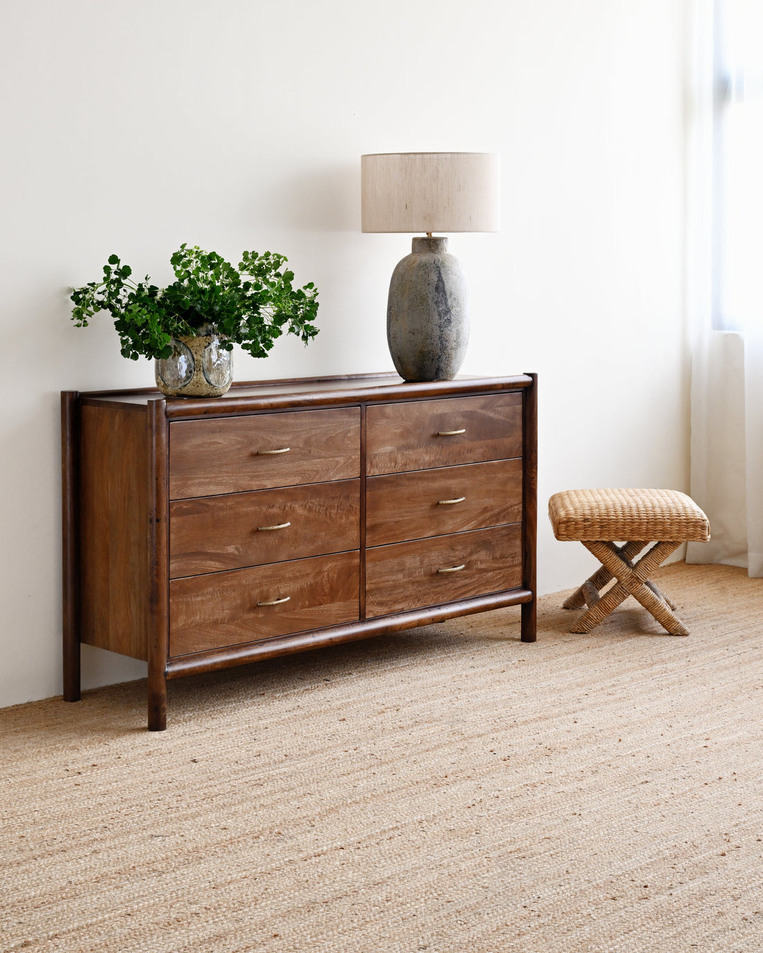 Wooden dresser with decorative items in a room with carpeted floor and white walls.