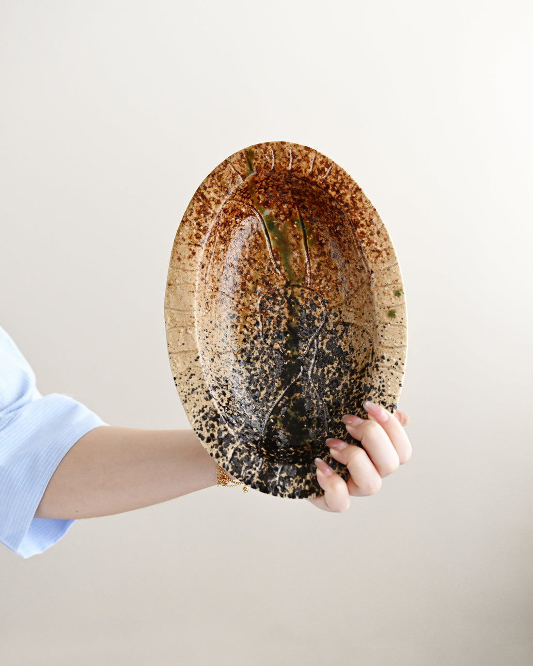 Person holding a ceramic plate with a textured surface against a plain background