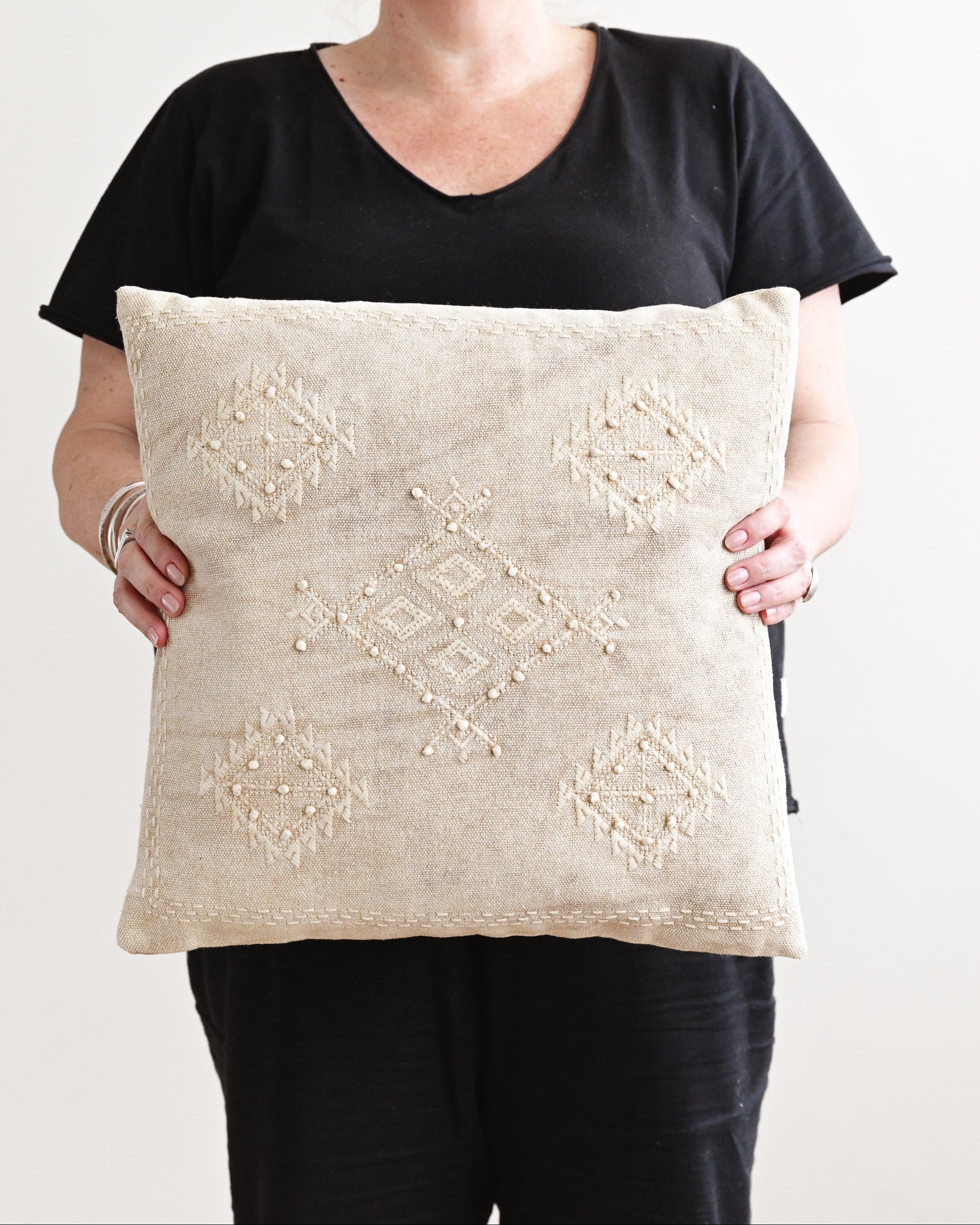 Person holding a decorative pillow with intricate patterns against a plain background