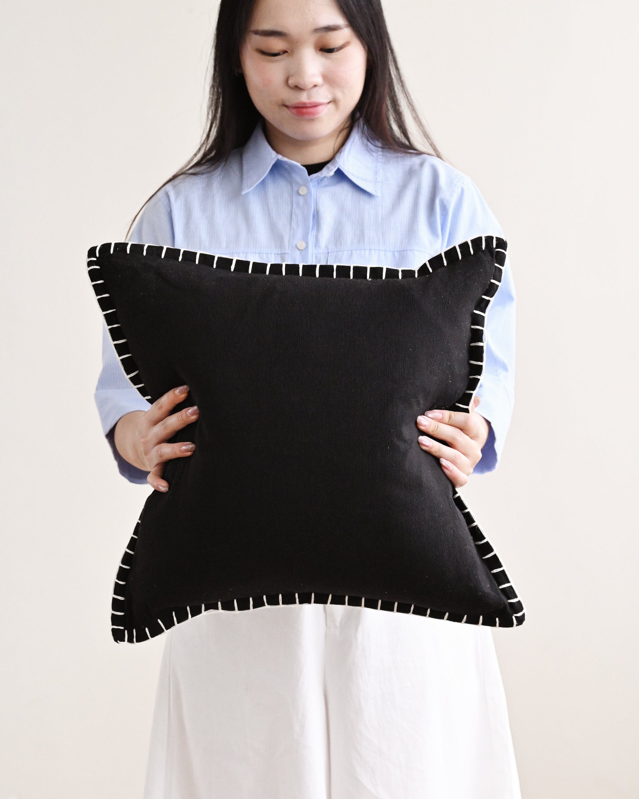 Person holding a black pillow with white trim against a plain background