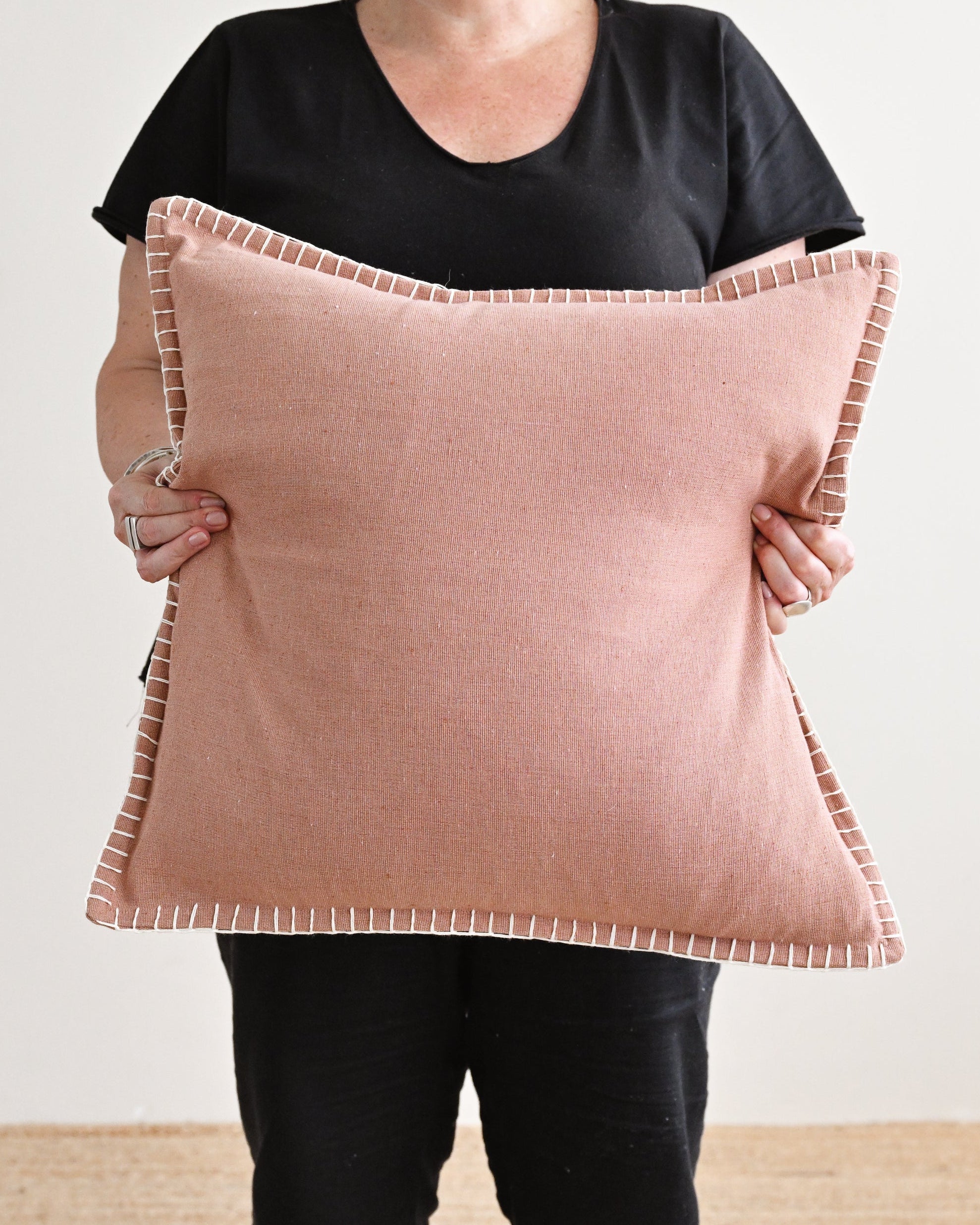 Person holding a large pink pillow against a plain background