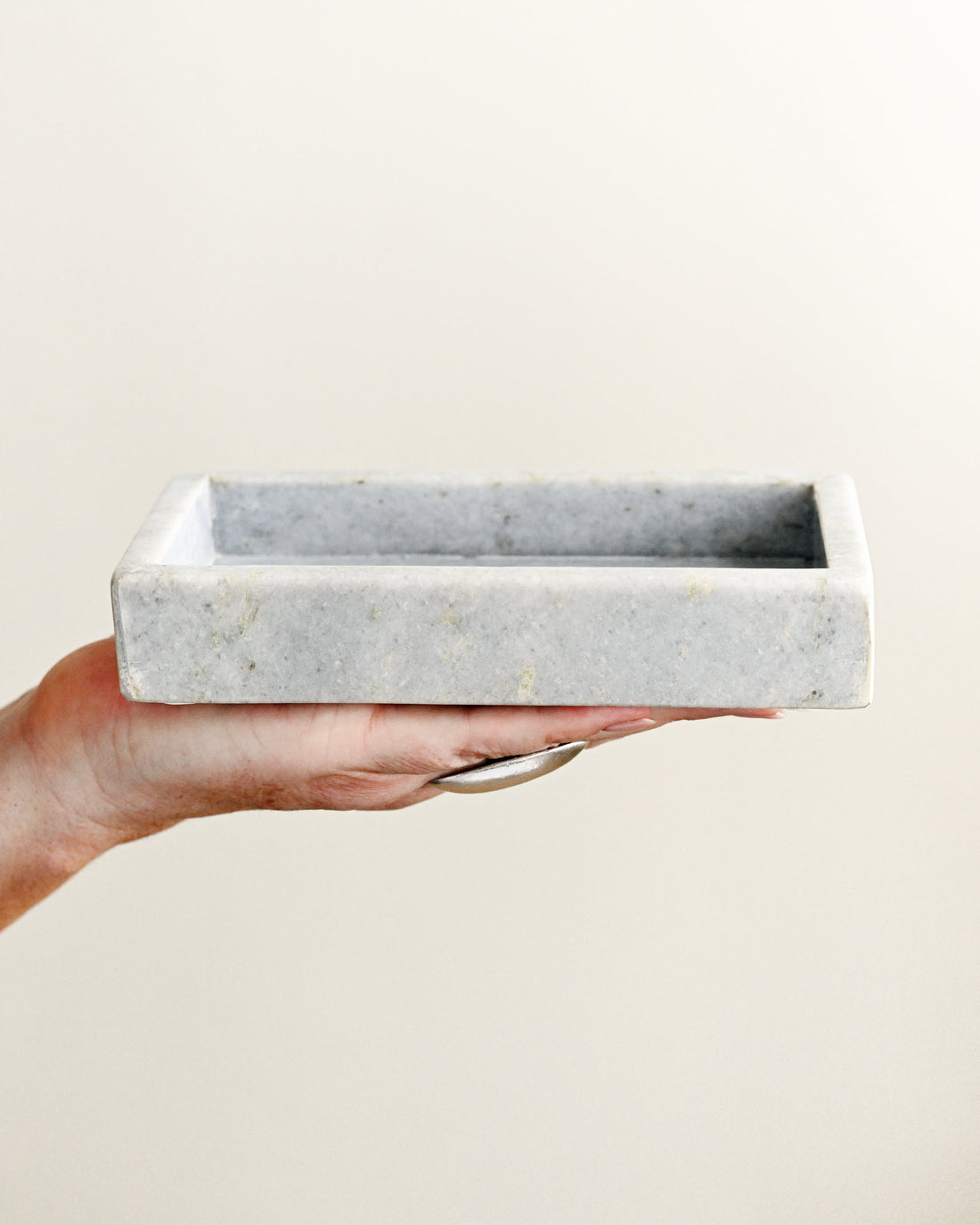 Hand holding a rectangular marble tray against a plain background