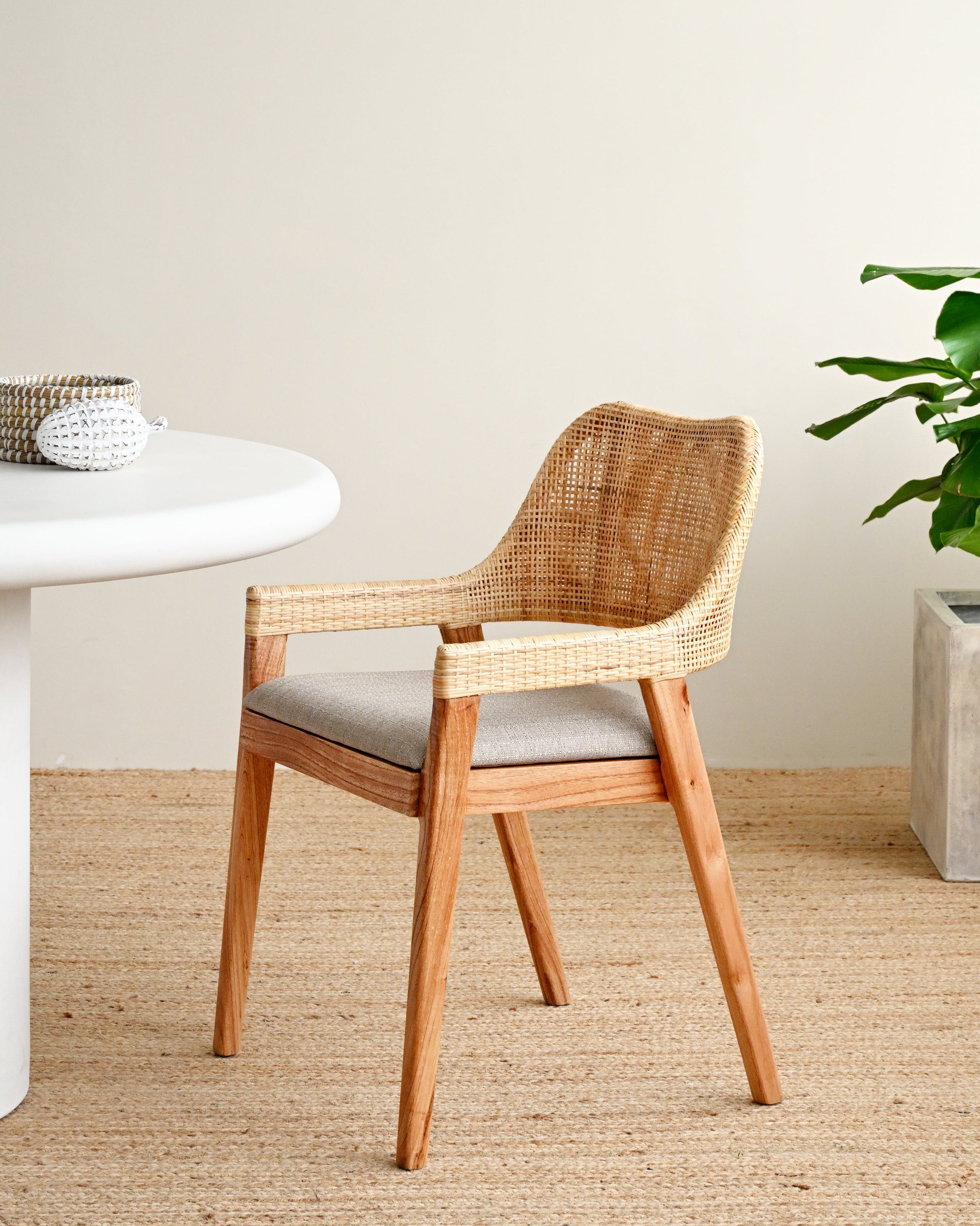 Wooden chair with a white cushion in a minimalistic room with a table and plant.