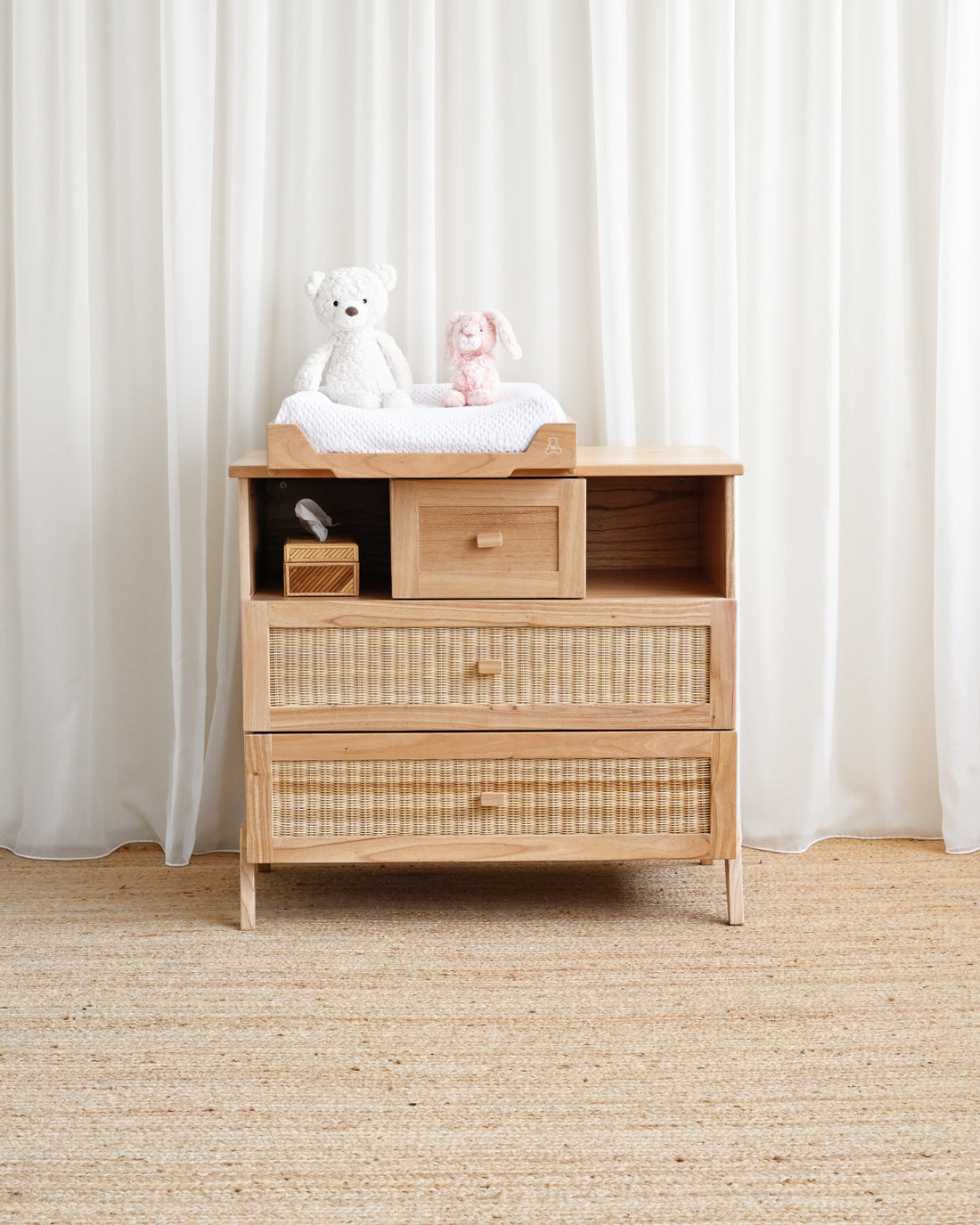 Wooden changing table with toys on top against a white curtain background