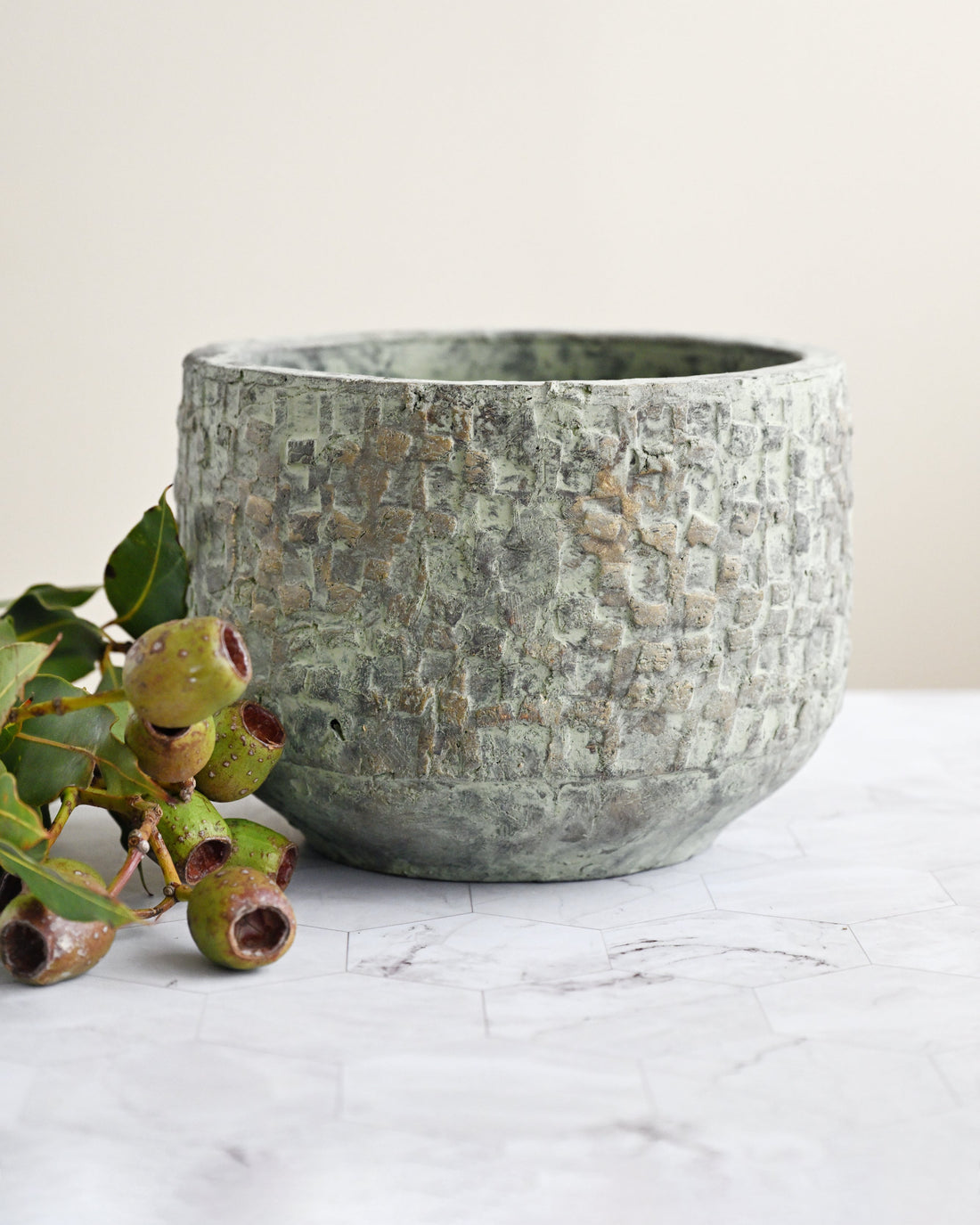 Textured ceramic pot on a marble surface with greenery
