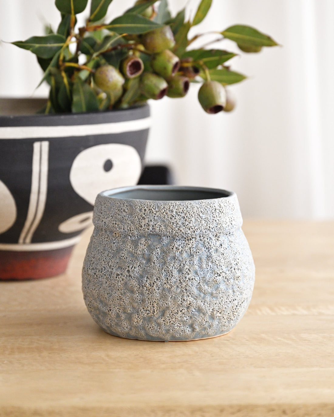 Textured gray pot on a wooden surface with another pot in the background