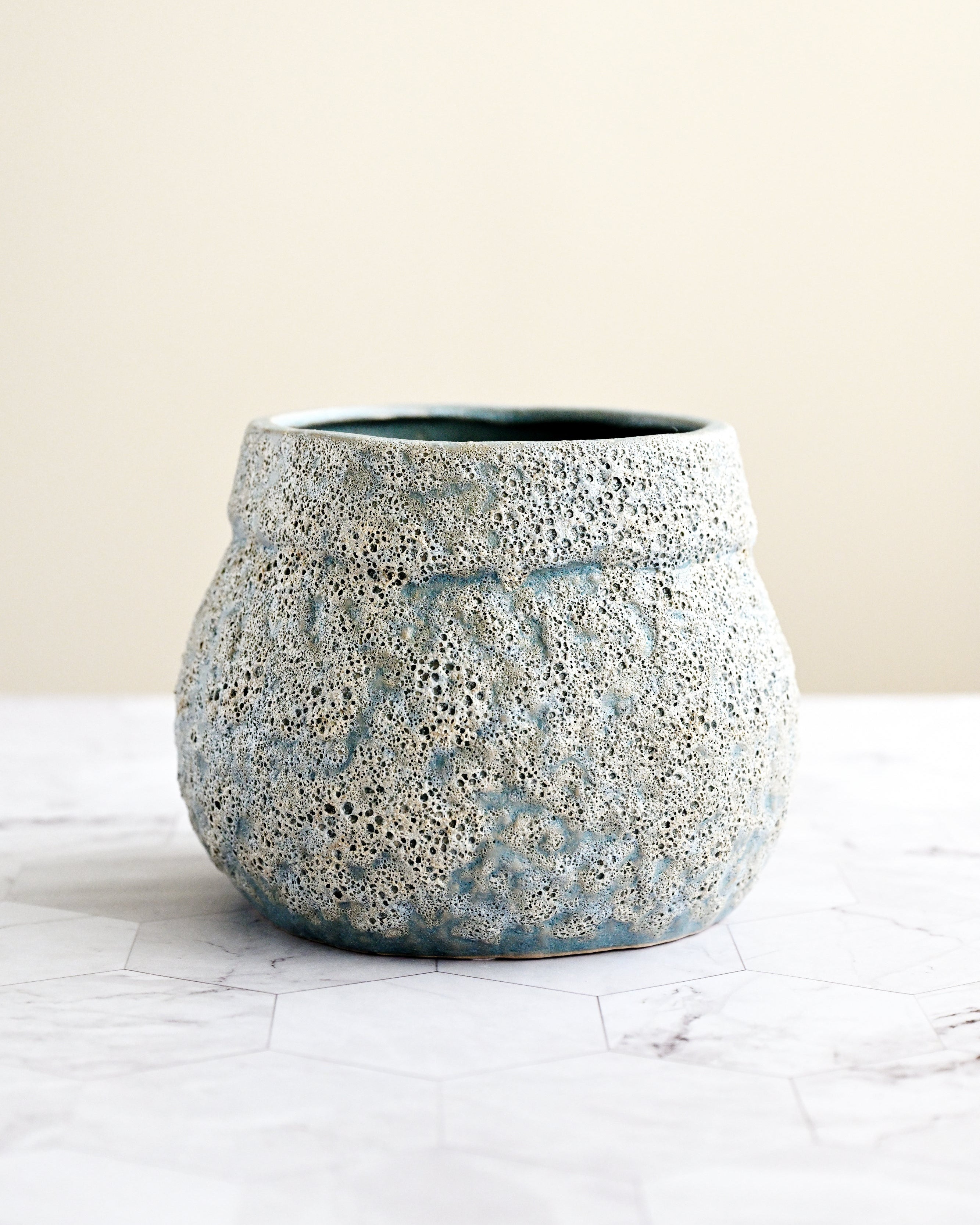 Speckled blue and gray ceramic pot on a white surface with a beige background