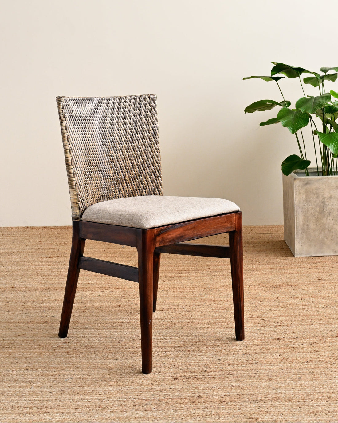 Wooden chair with a woven backrest and beige cushion next to a potted plant on a wooden floor.