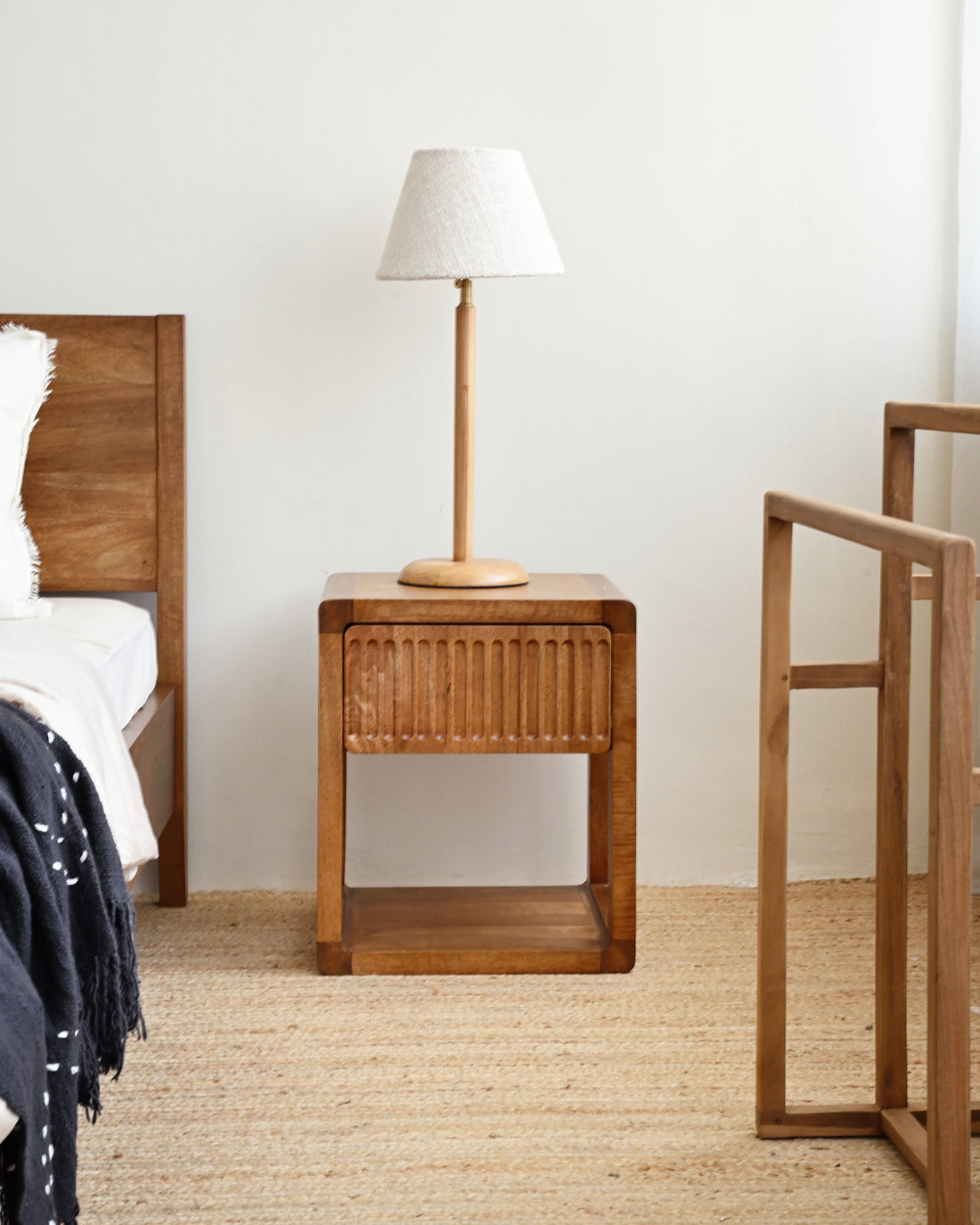 Wooden nightstand with lamp next to a bed in a bedroom setting