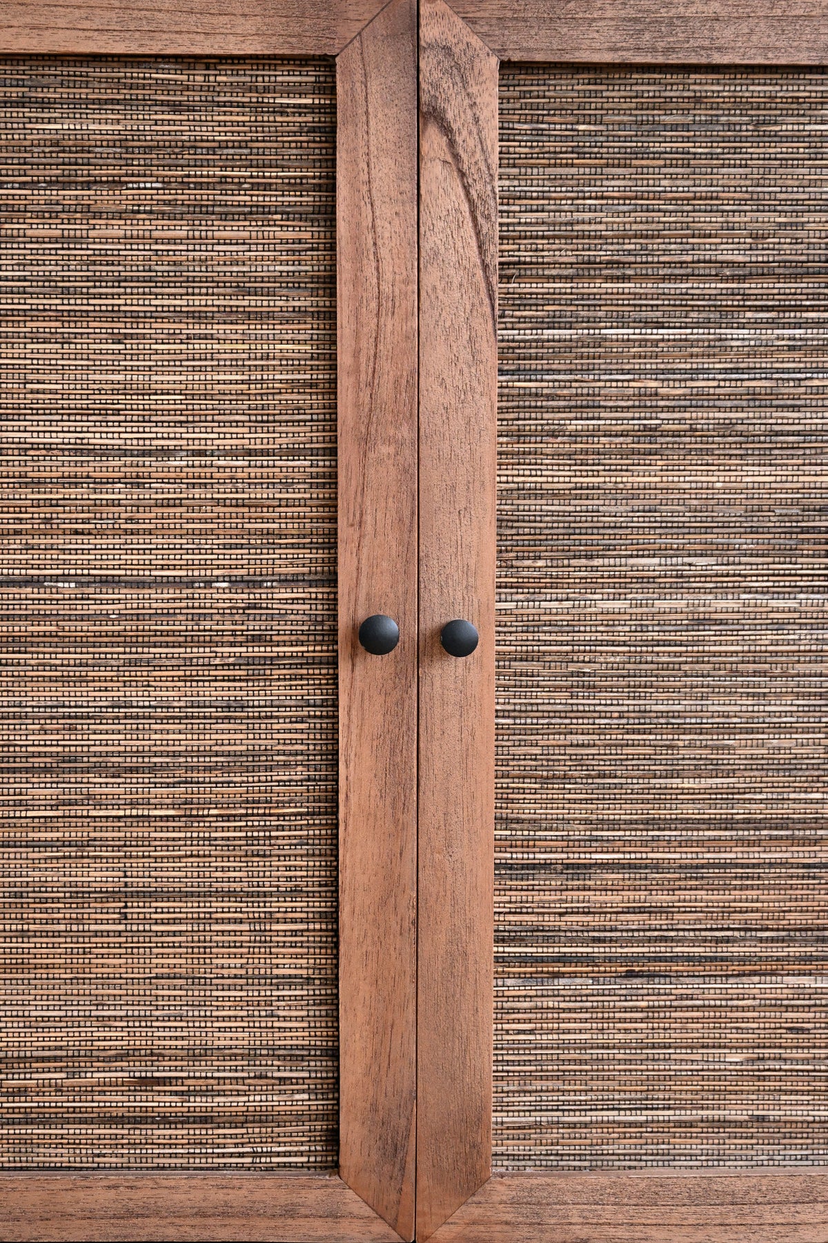 A close-up of a wooden cabinet door with woven rattan panels on both sides and two round black knobs in the center.