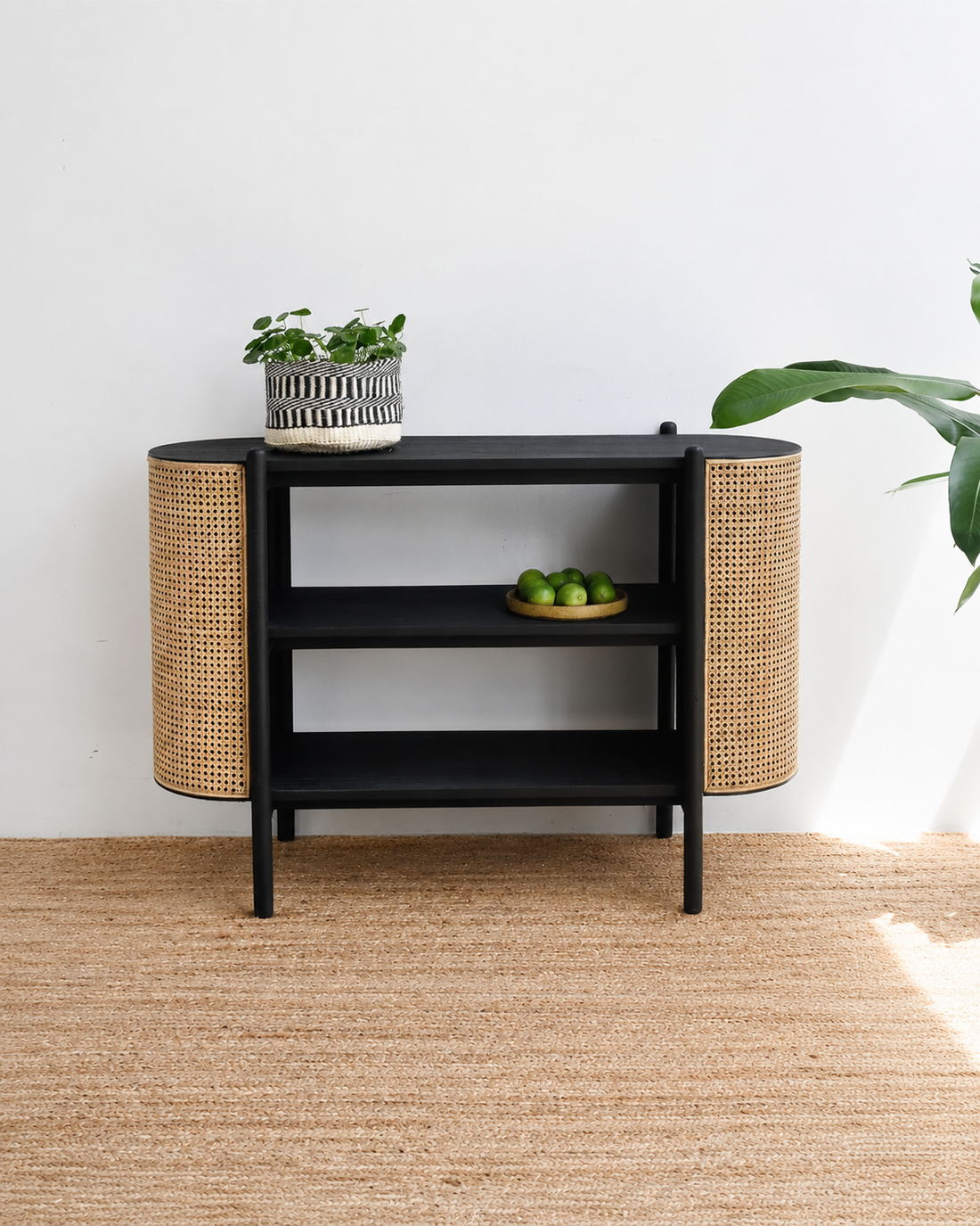 Black side table with wicker accents in a room with a white wall and wooden floor.