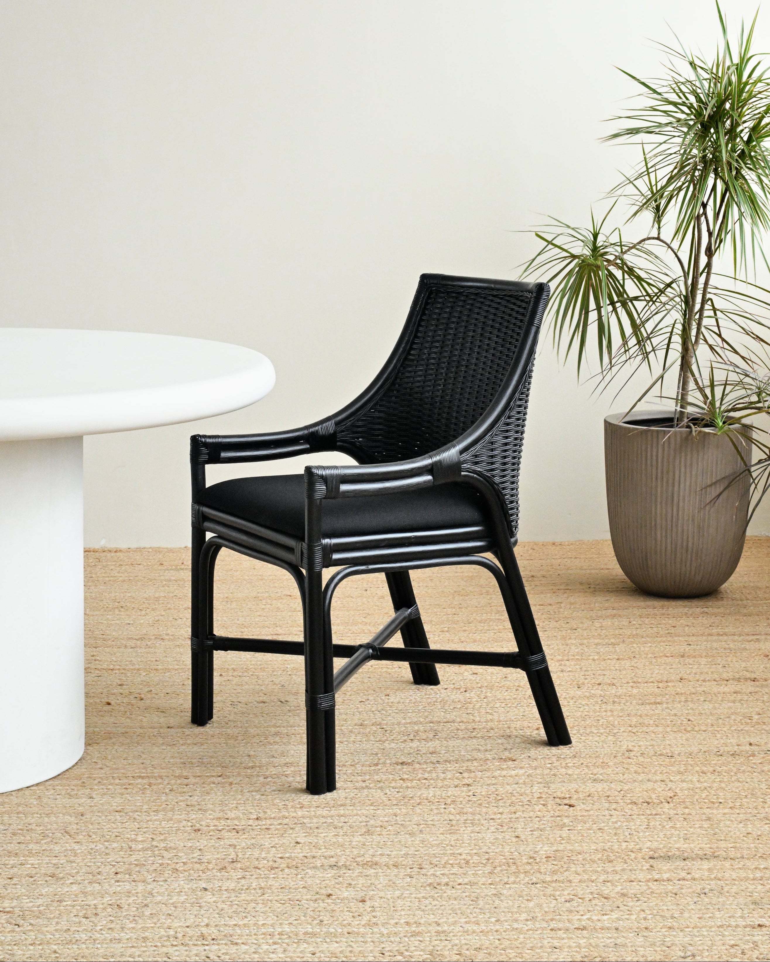 Black wicker chair next to a white table with a plant in the background