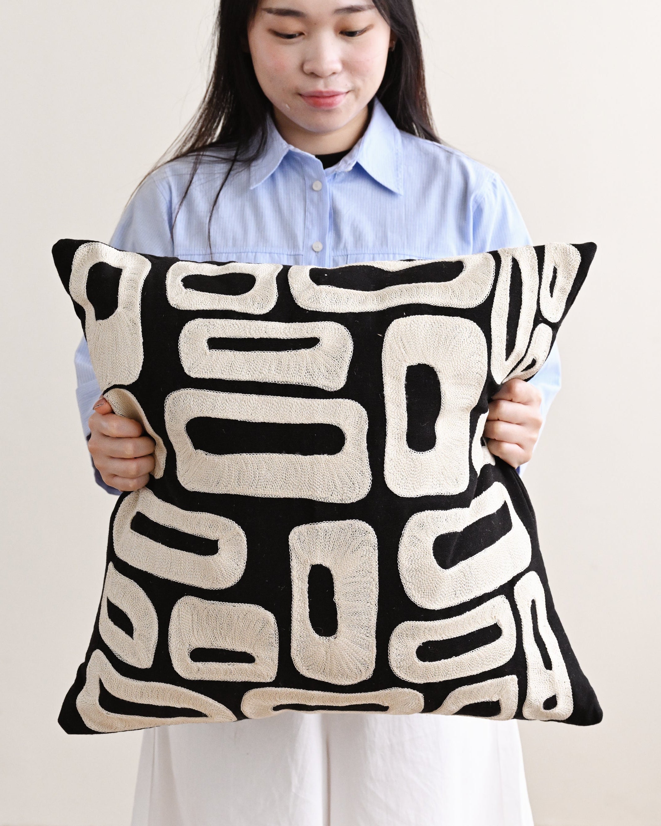 Person holding a black and white patterned pillow against a plain background