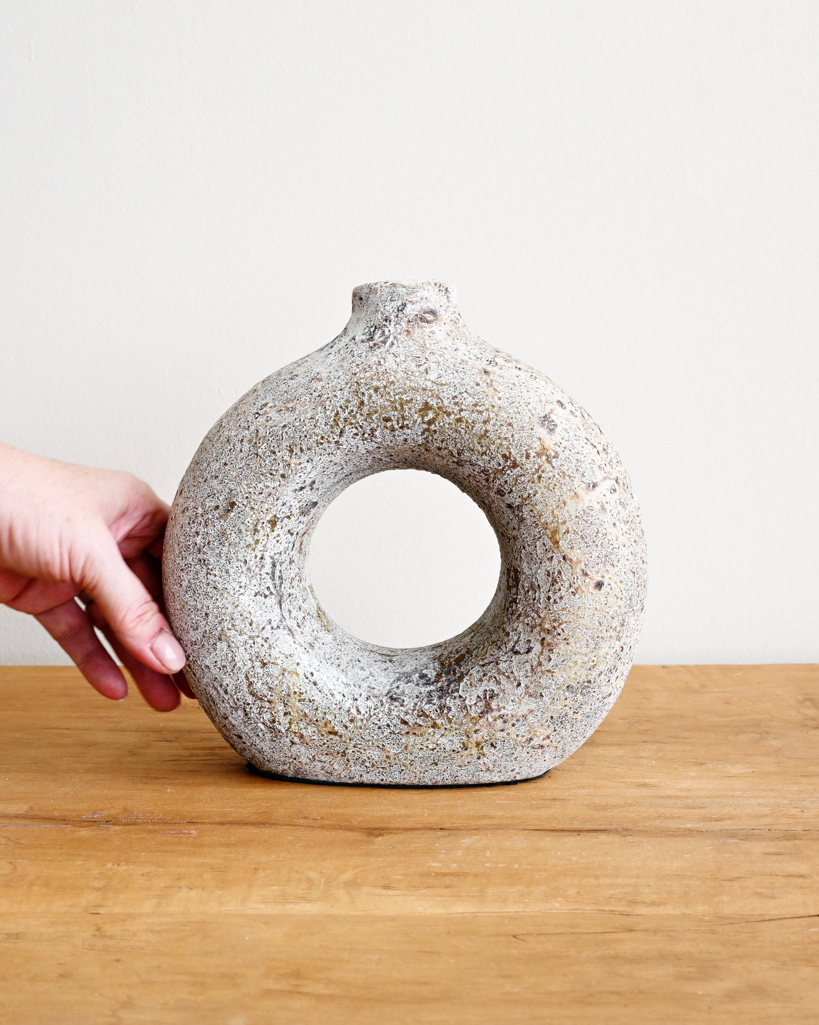Hand holding a textured ceramic vase on a wooden surface with a white background