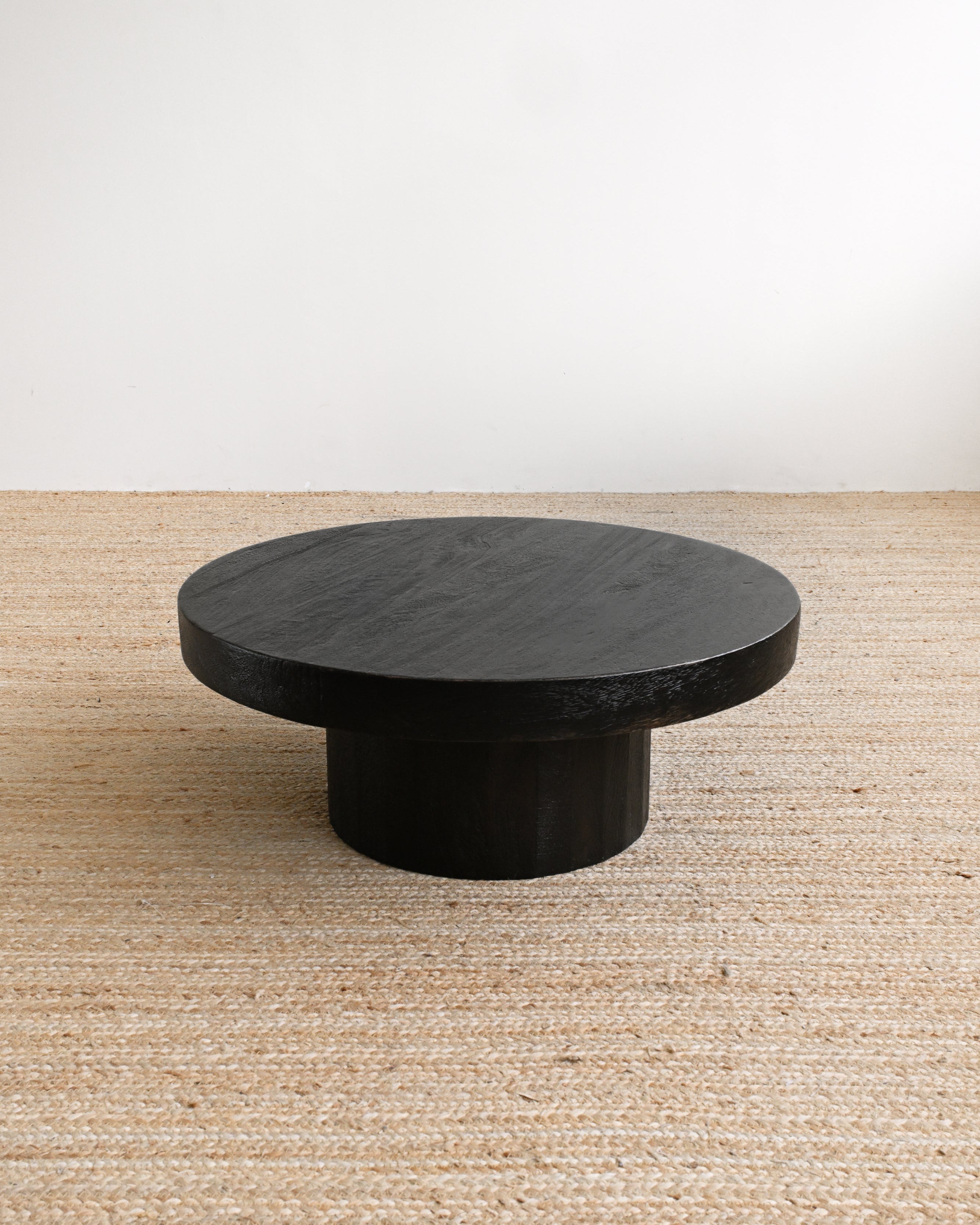 Round black stone table on a beige carpet with a white wall background