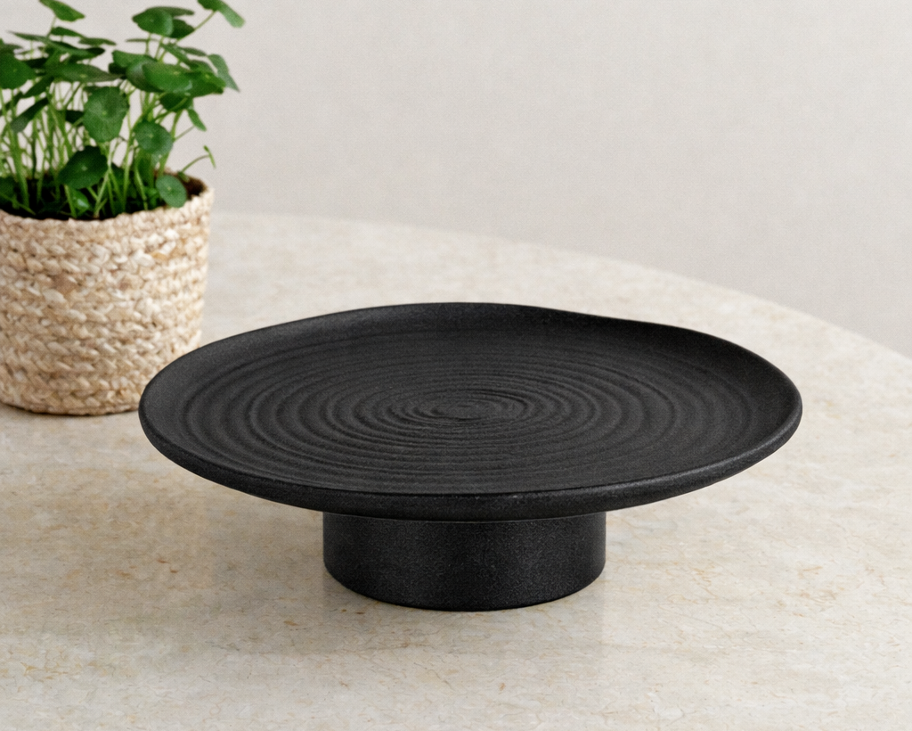 Black decorative plate on a light surface with a plant in the background