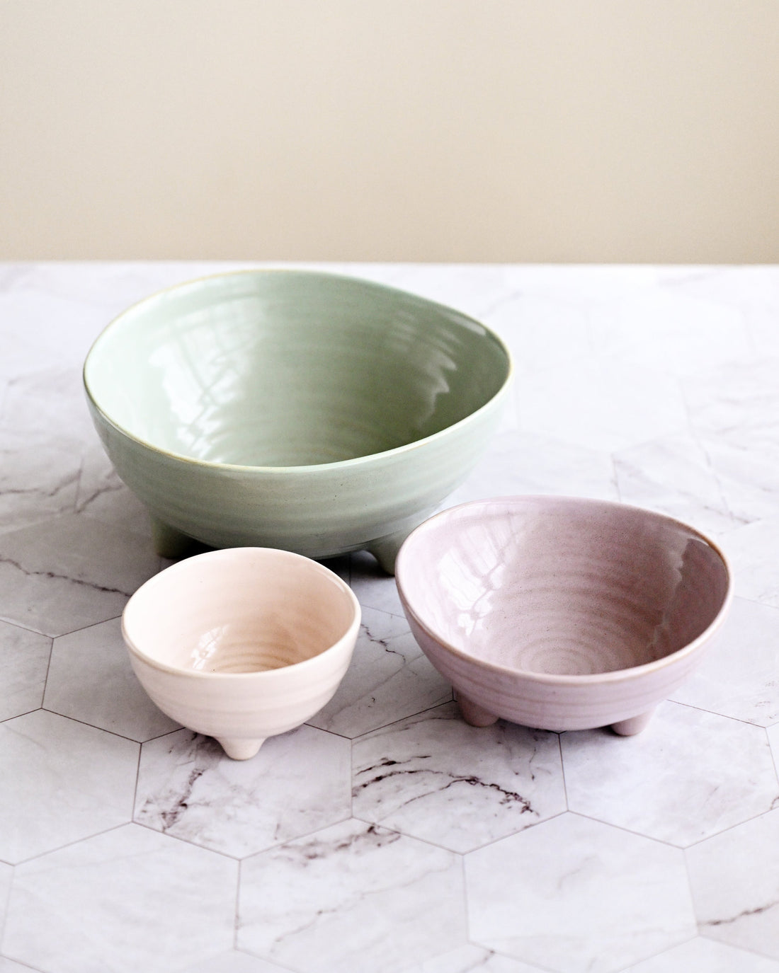 Three ceramic bowls in green, pink, and white on a marble surface.