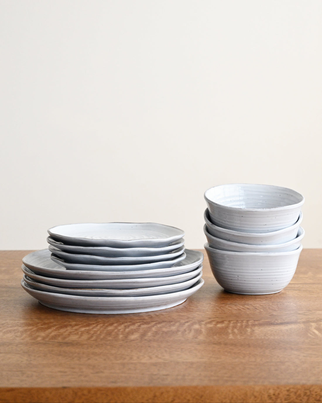 Stacks of gray ceramic plates and bowls on a wooden surface with a light gray background
