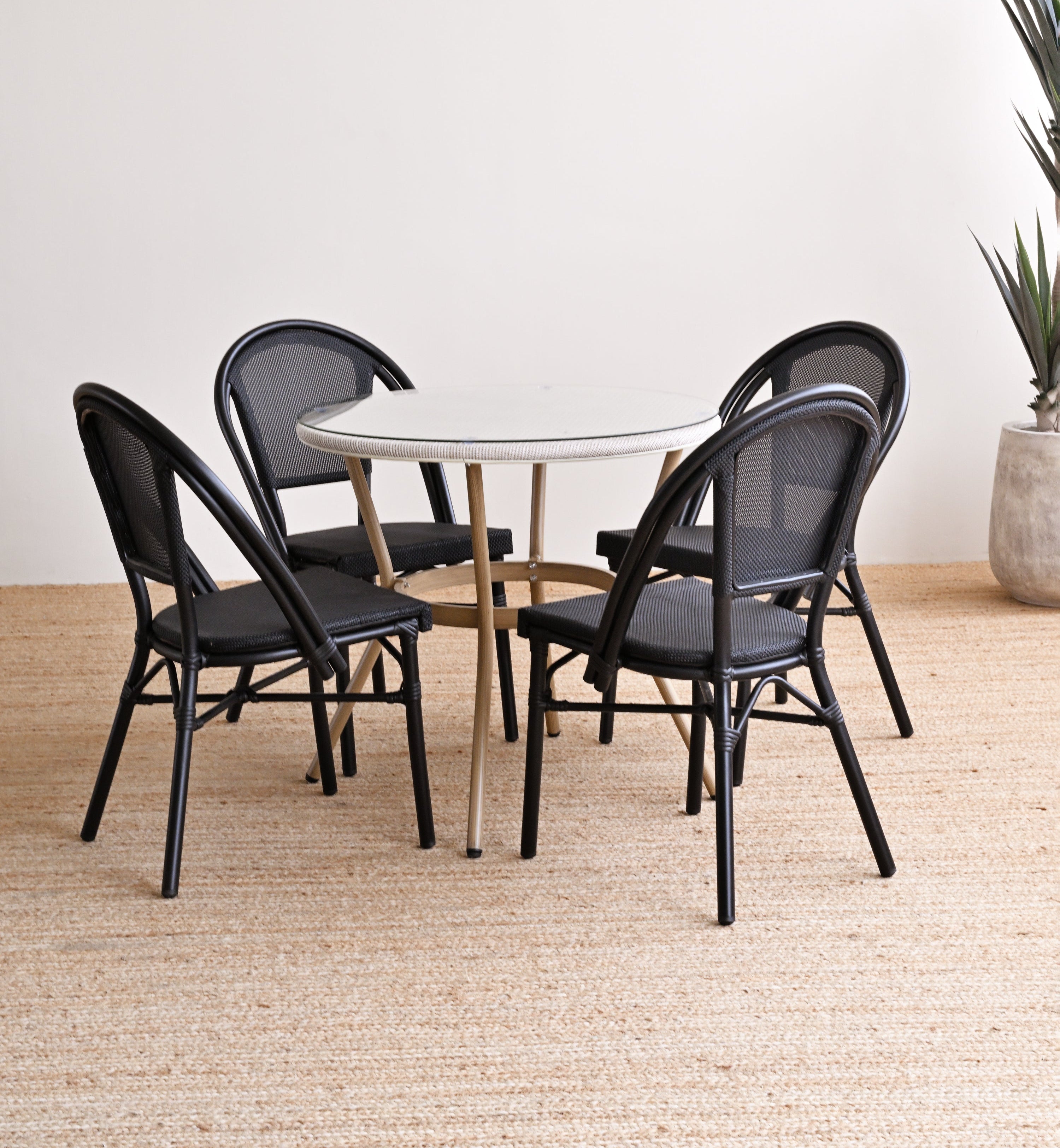 Round table with four black chairs on a wooden floor against a white wall.