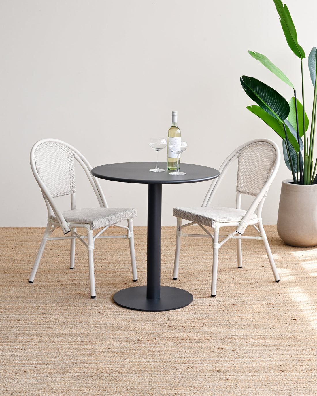Two chairs around a round black table with a plant and bottle on a beige rug.