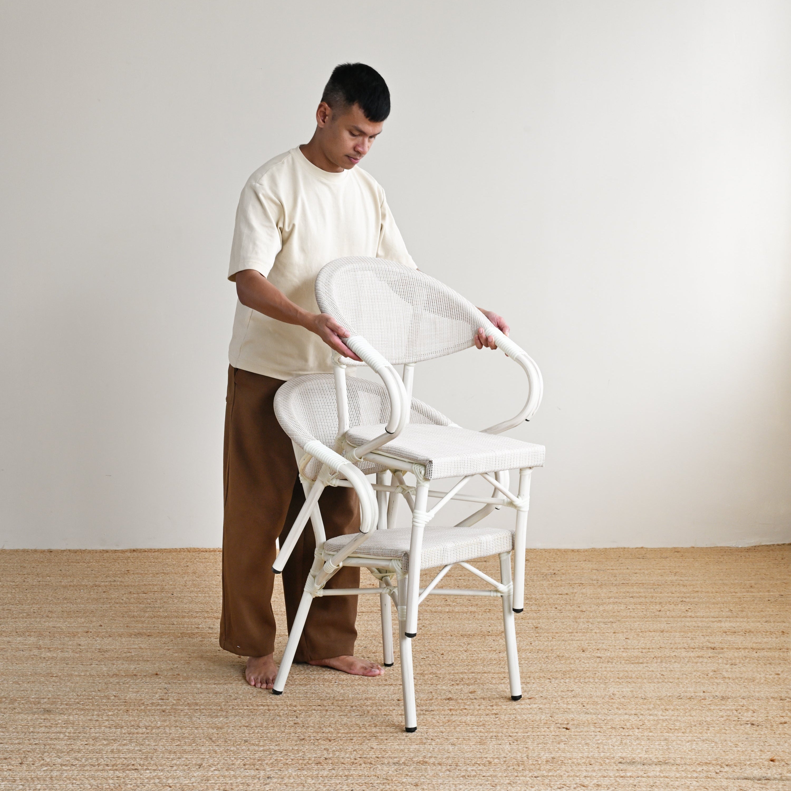 Person arranging white chairs in a minimalistic room with a plain background