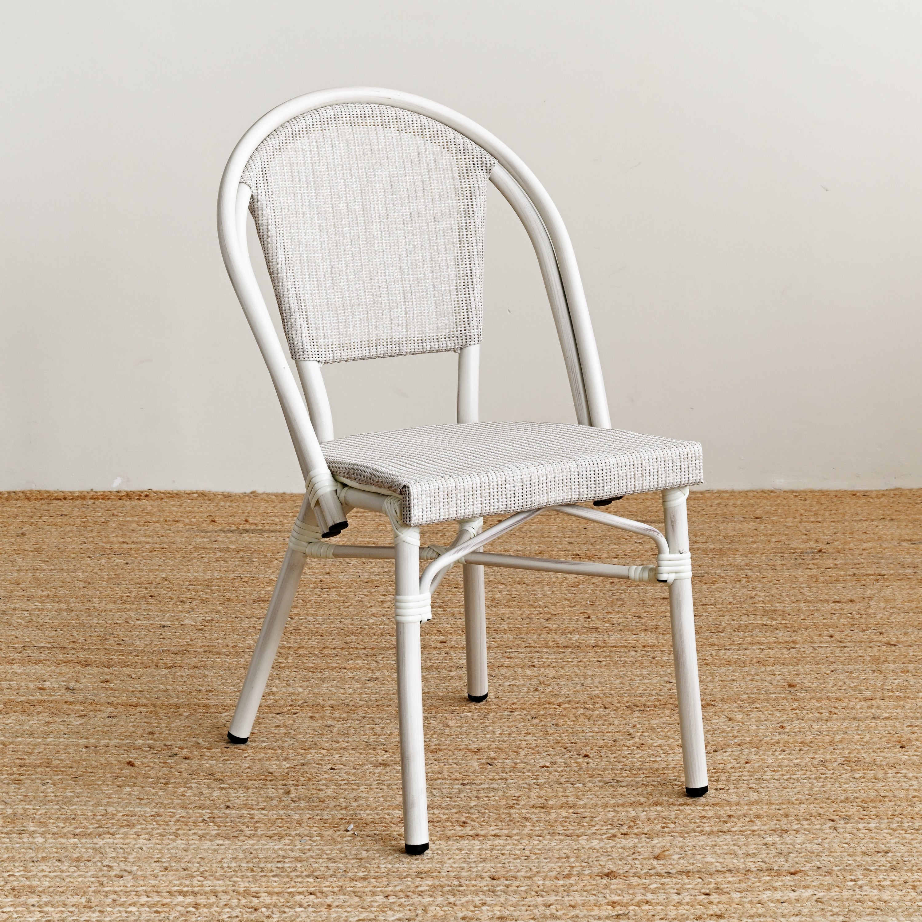 White metal chair with woven seat on a textured beige floor and light gray wall
