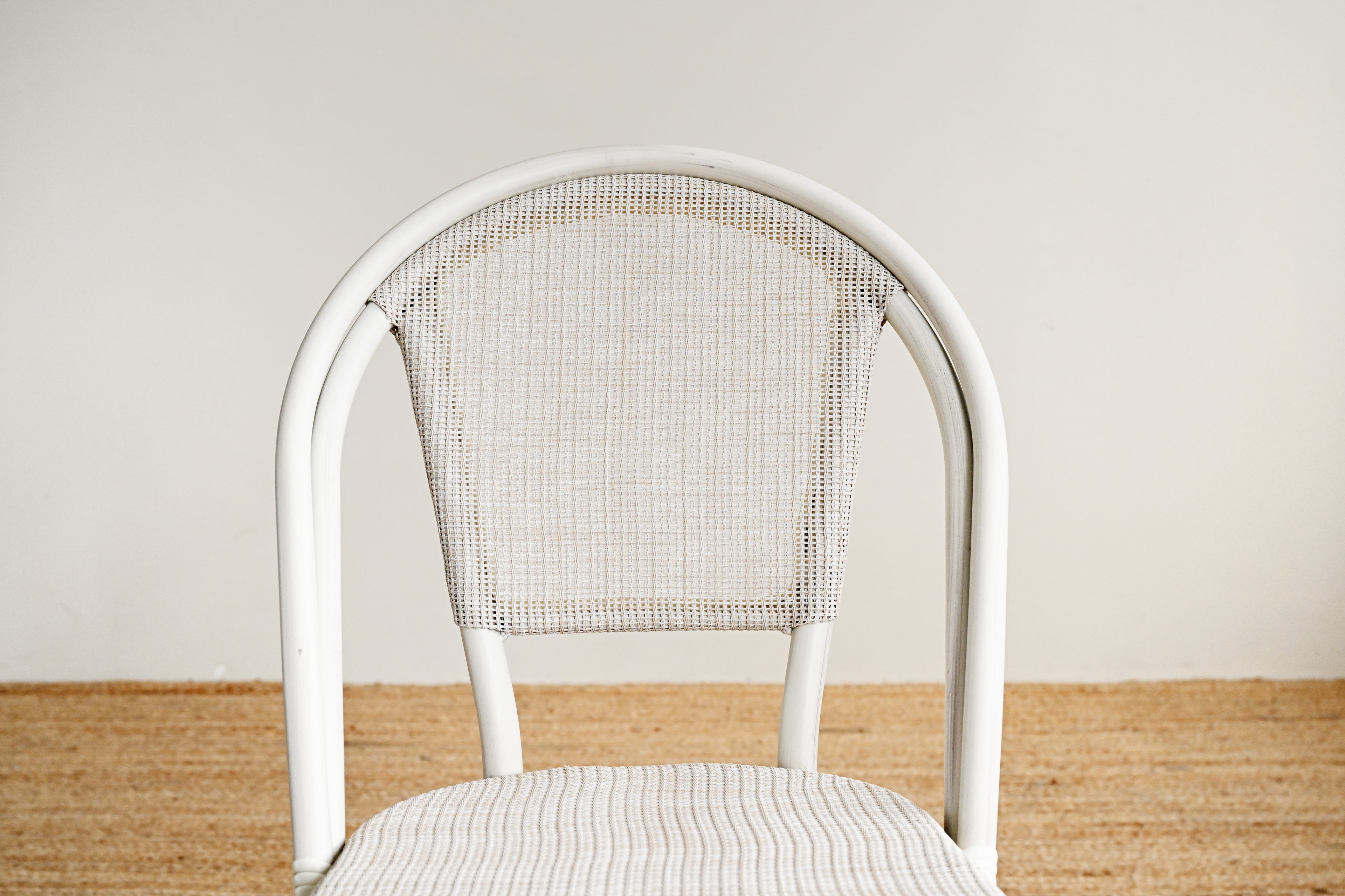 White chair with woven backrest on a wooden floor against a plain wall