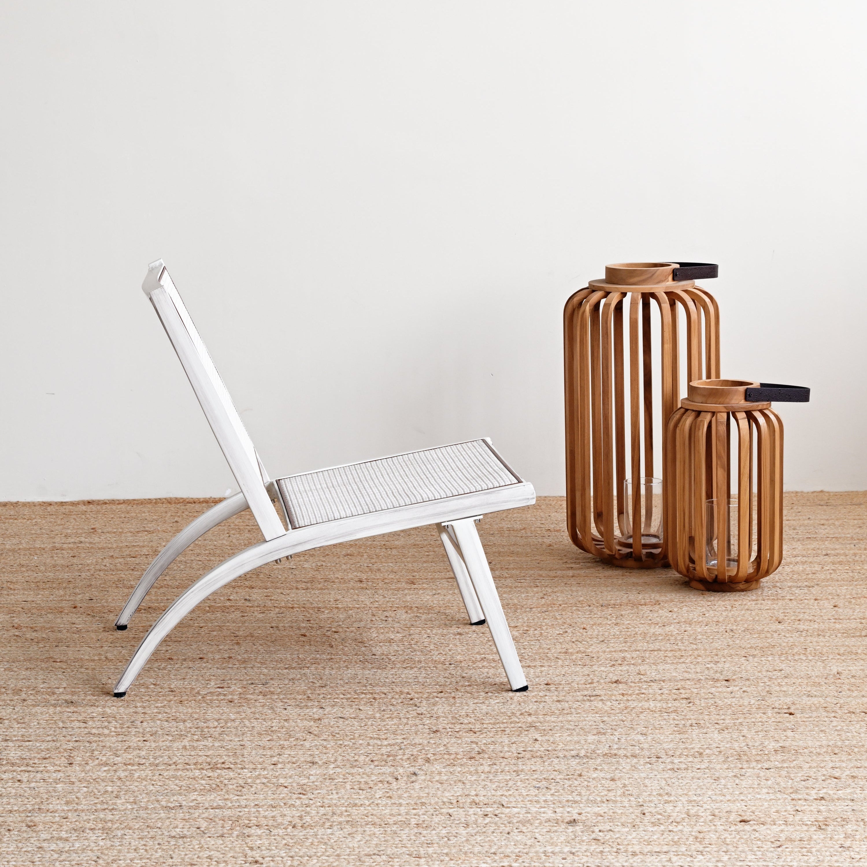 White chair with woven seat and backrest on a beige carpet, accompanied by two wooden vases against a white wall.