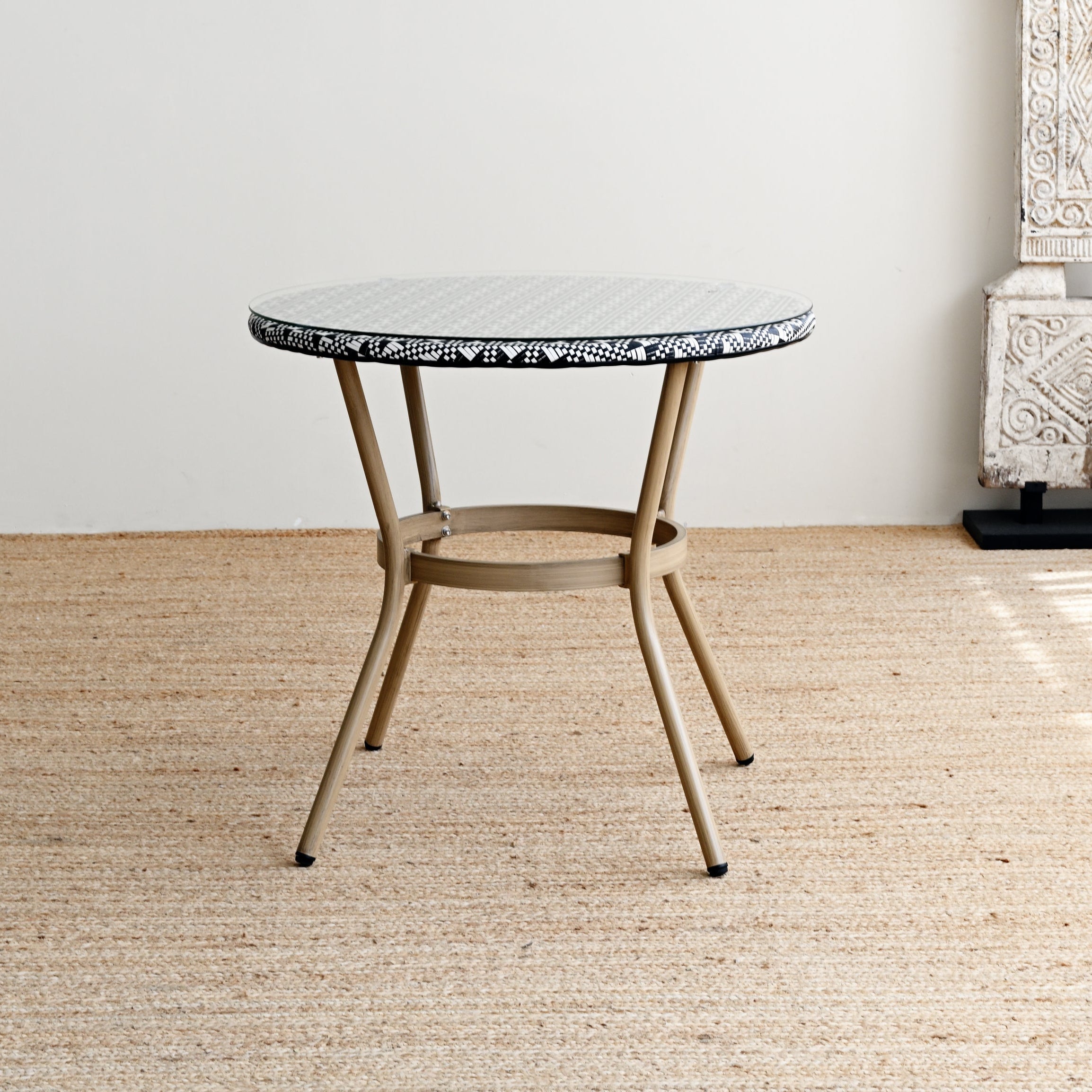 Small round table with a textured surface next to a tall white sculpture on a wooden floor.