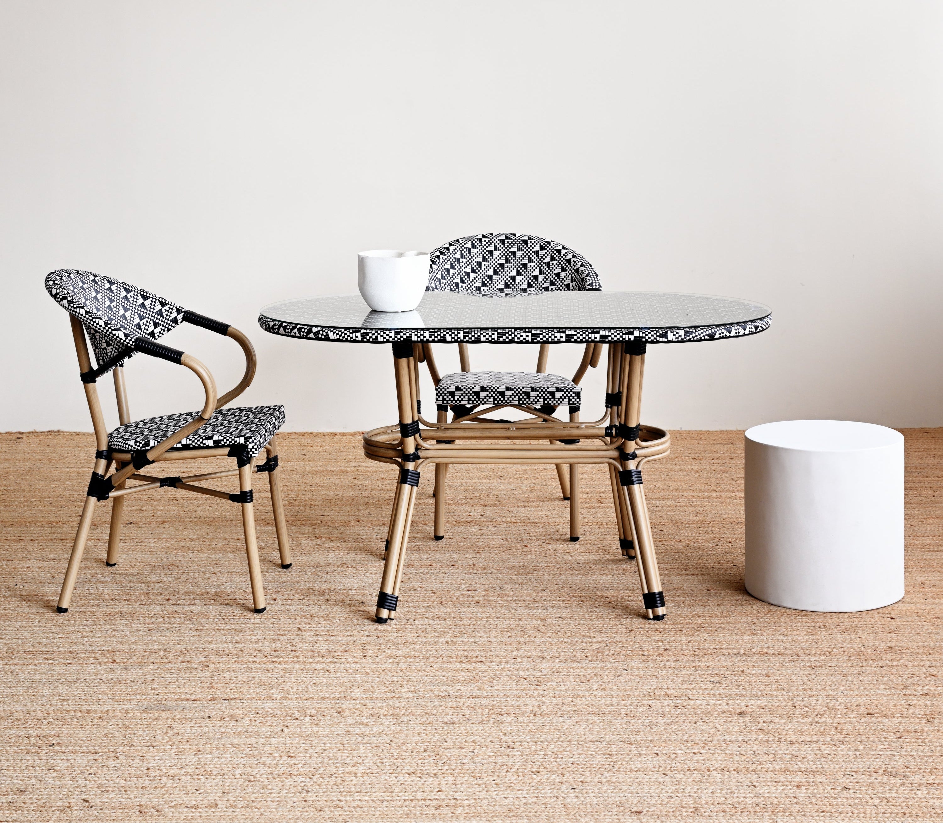 Round glass table with two chairs on a wooden floor against a white wall