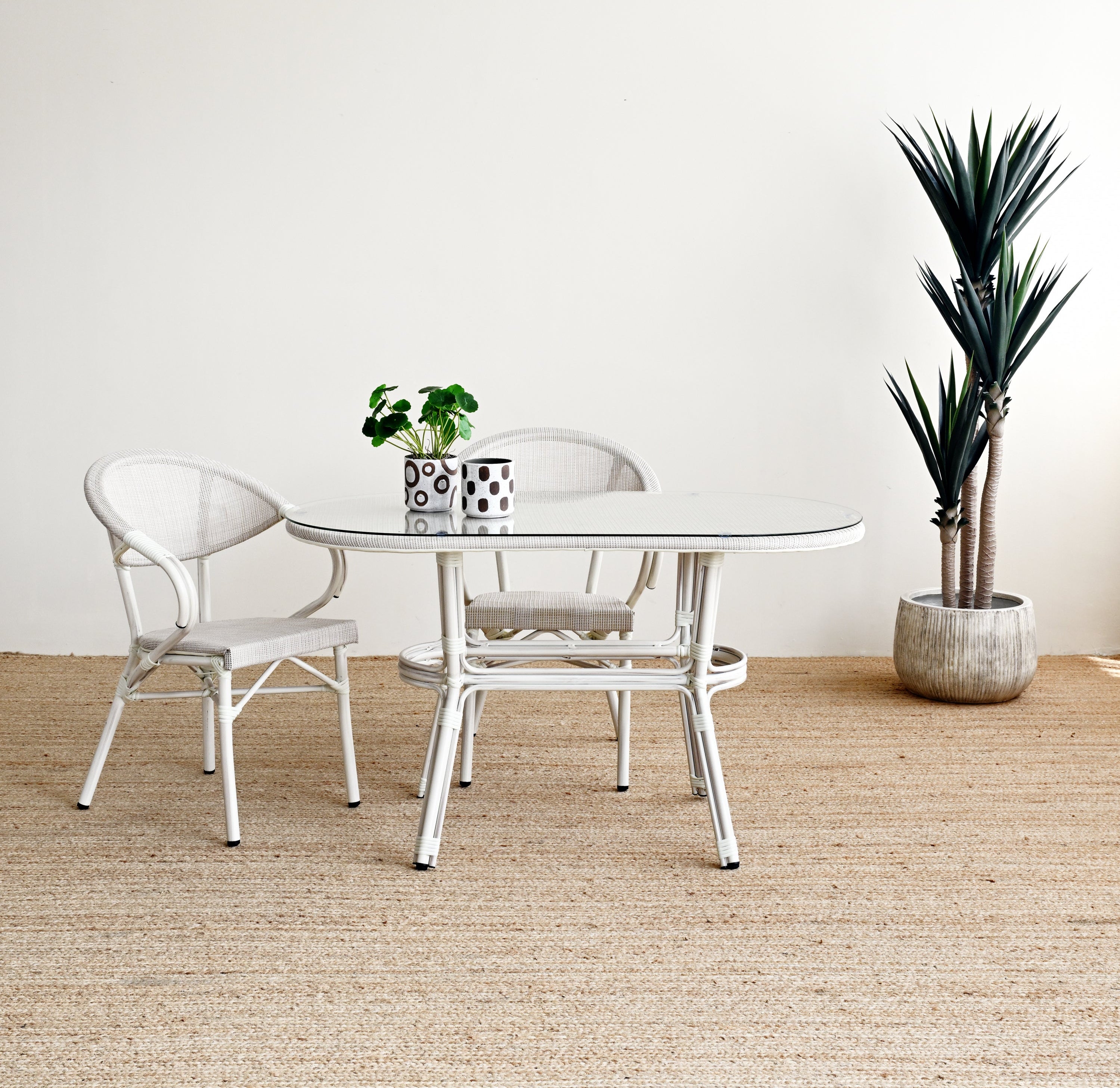 Dining area with a round glass table and two chairs on a textured beige floor.