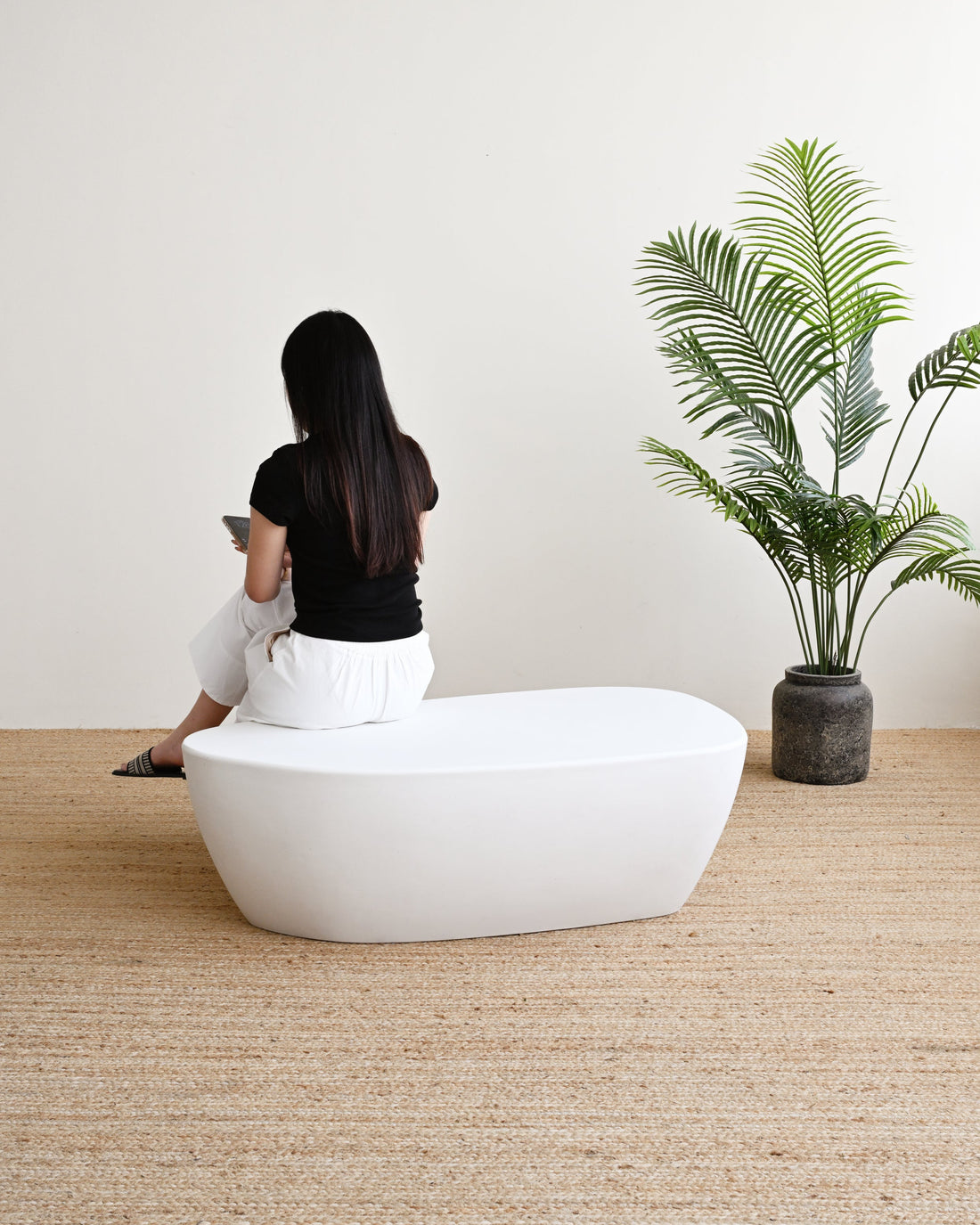 Person sitting on a white bench in a minimalistic room with a plant.