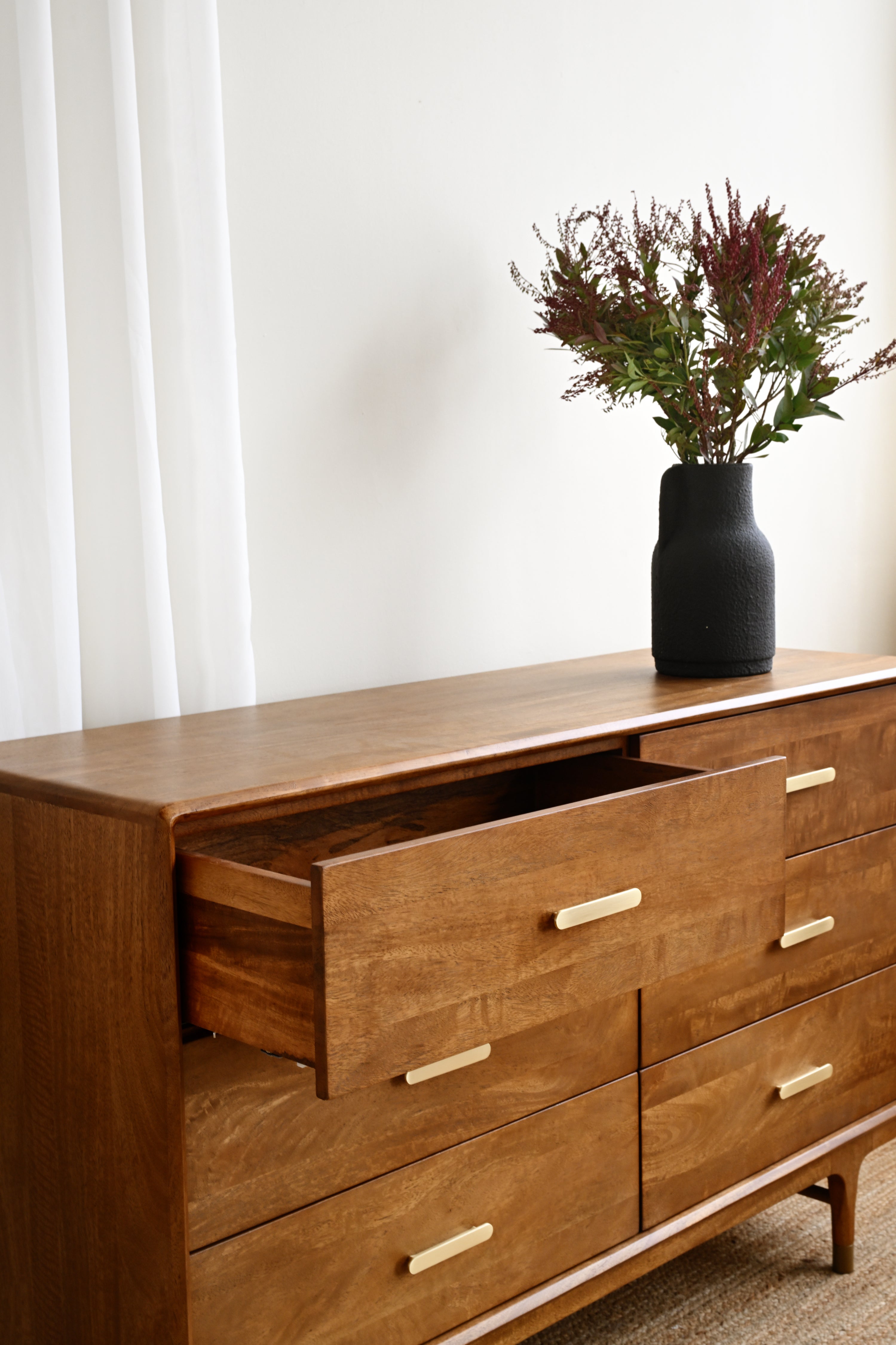 Wooden dresser with open drawer and vase of flowers on a white background
