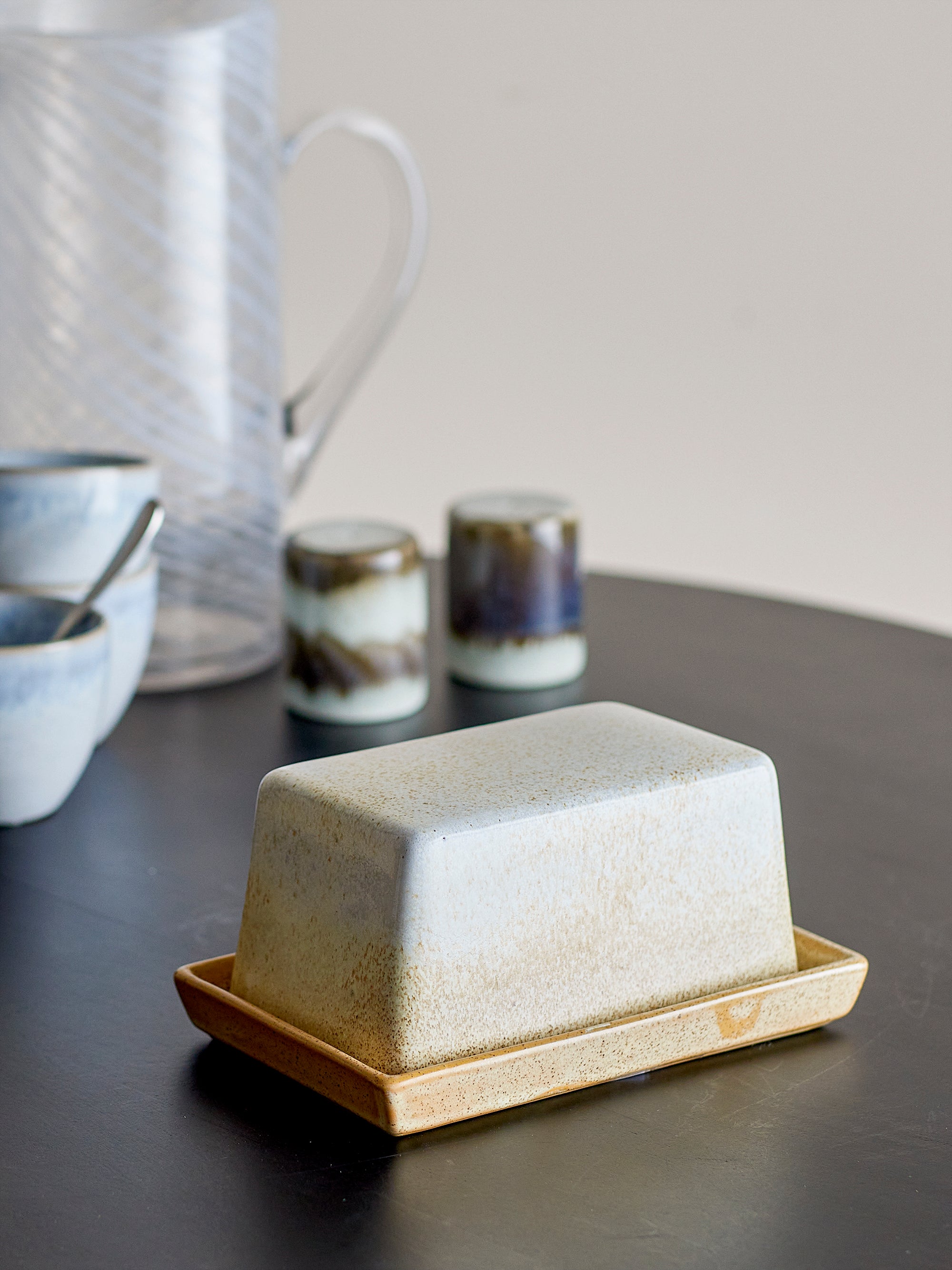 Ceramic butter dish on a wooden tray with a blurred background of kitchen items.