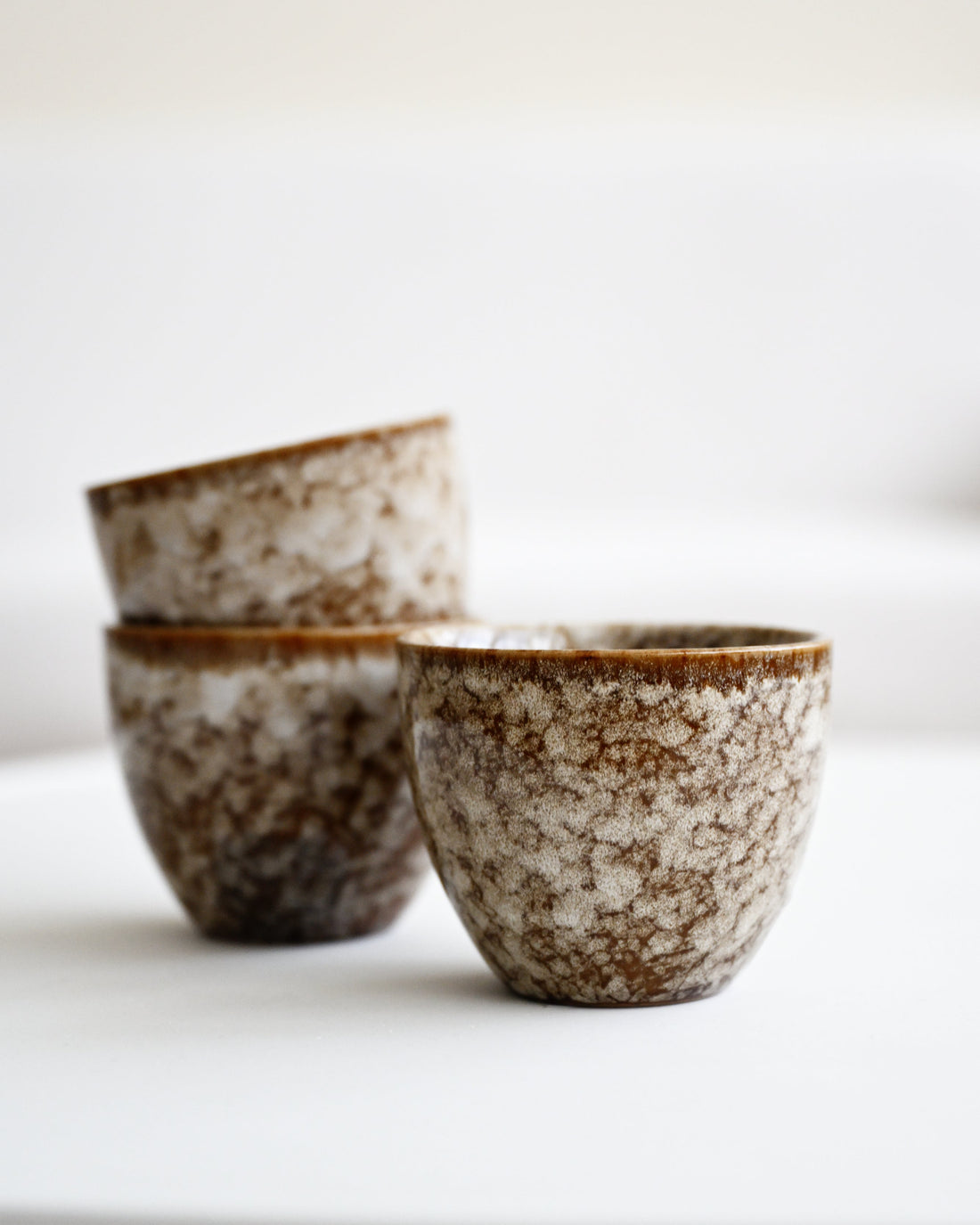 Three ceramic cups with speckled glaze on a white surface and background