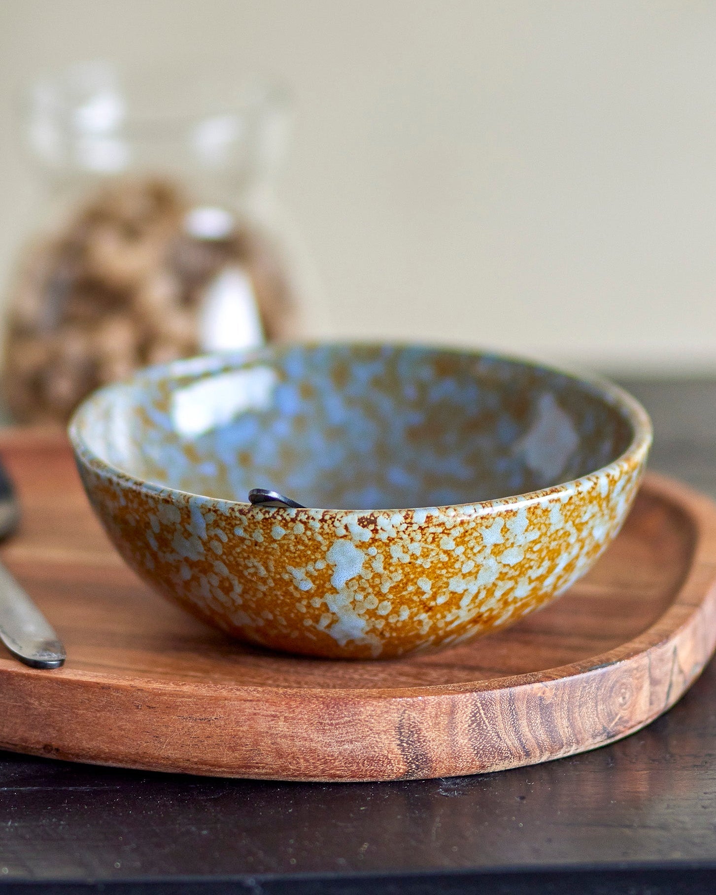 Ceramic bowl with gold and blue glaze on a wooden tray with a neutral background