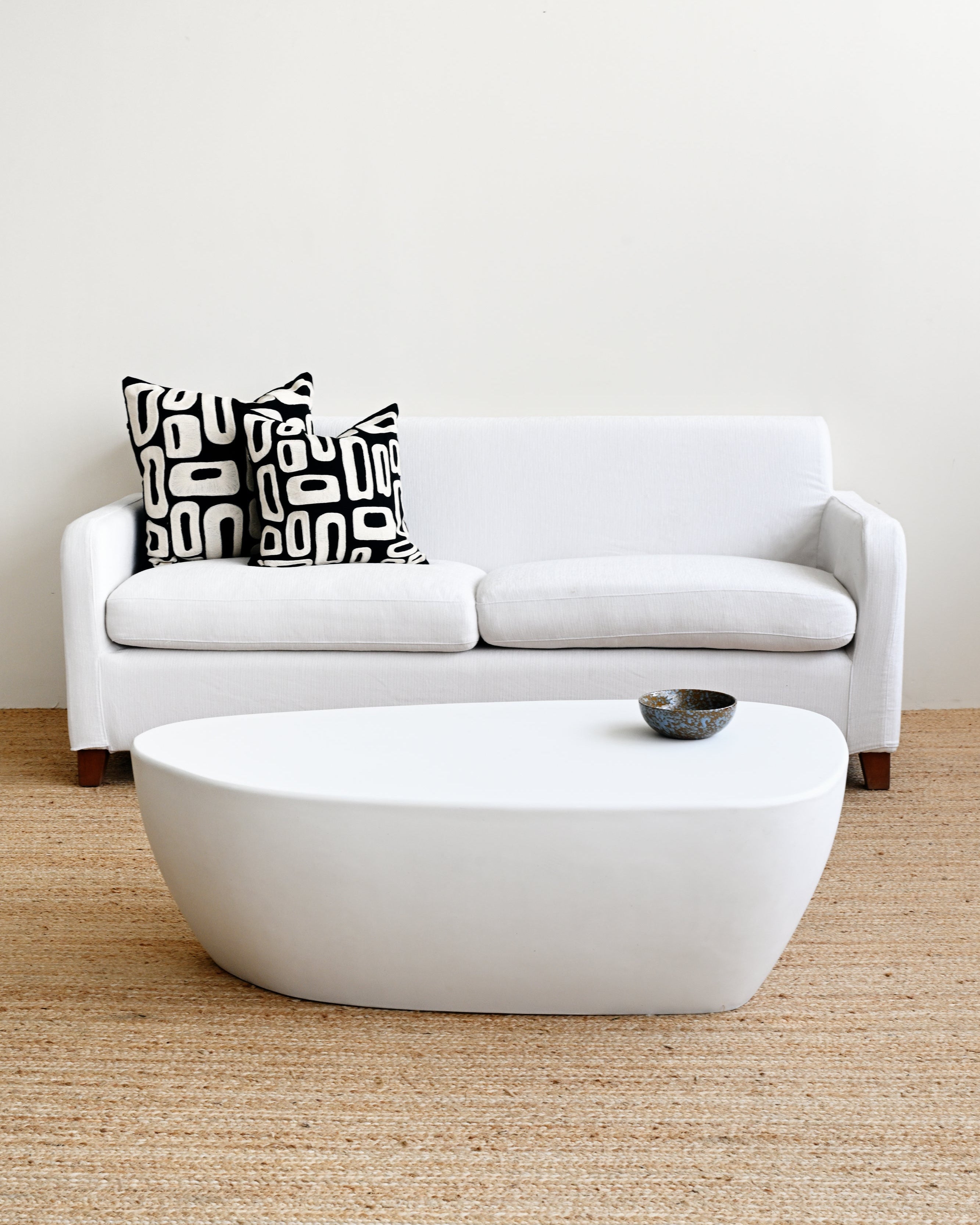 White sofa with a patterned pillow and a matching white coffee table in a minimalistic living room.