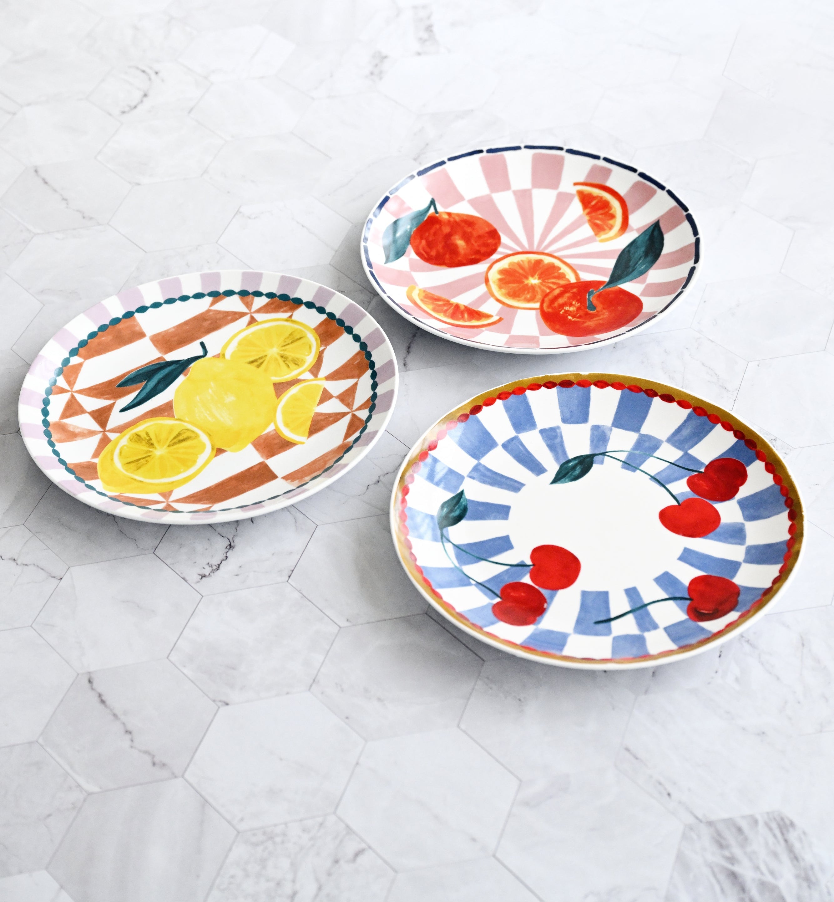 Three colorful ceramic plates with fruit designs on a marble surface.