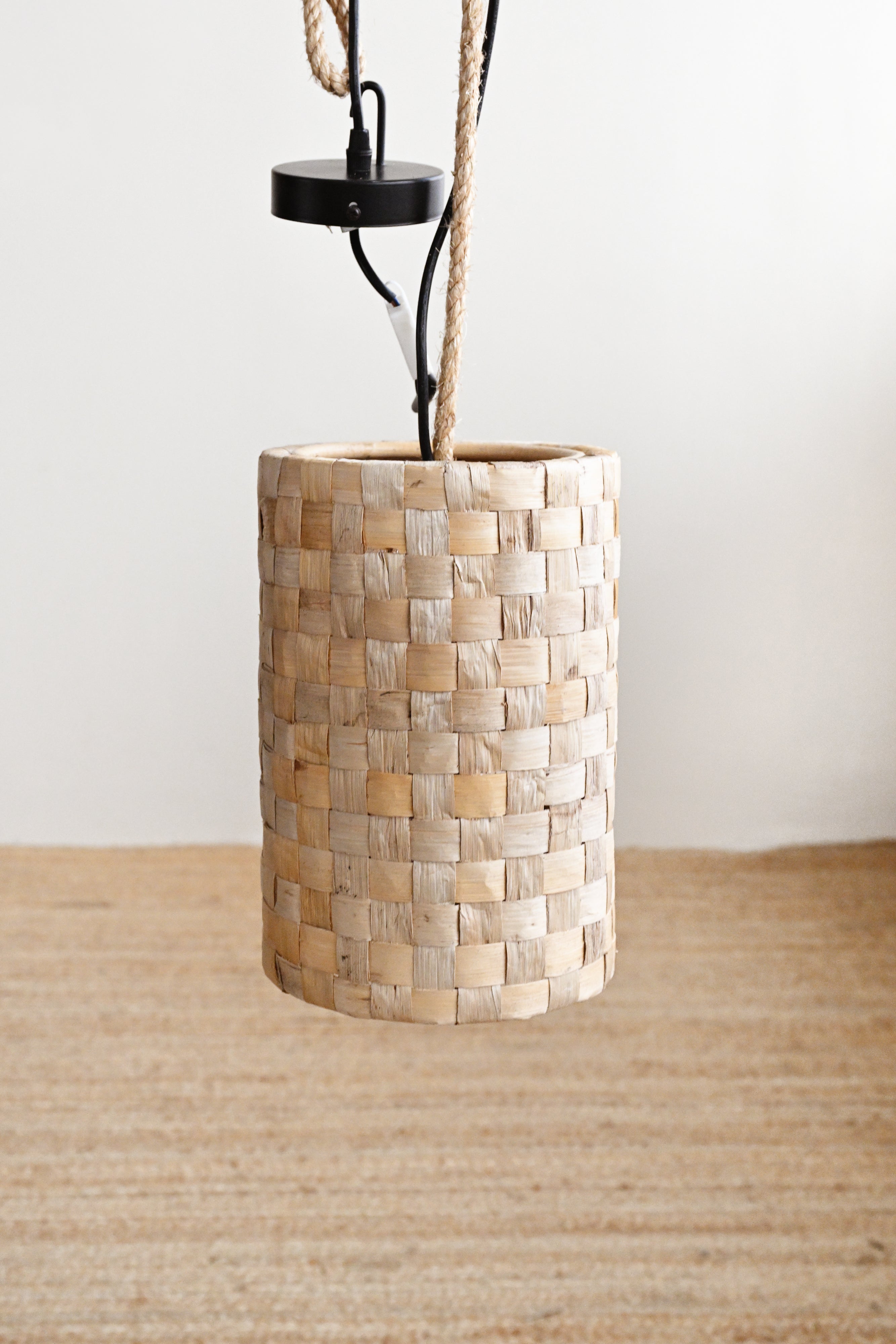 Pendant light with woven wooden shade on a neutral background