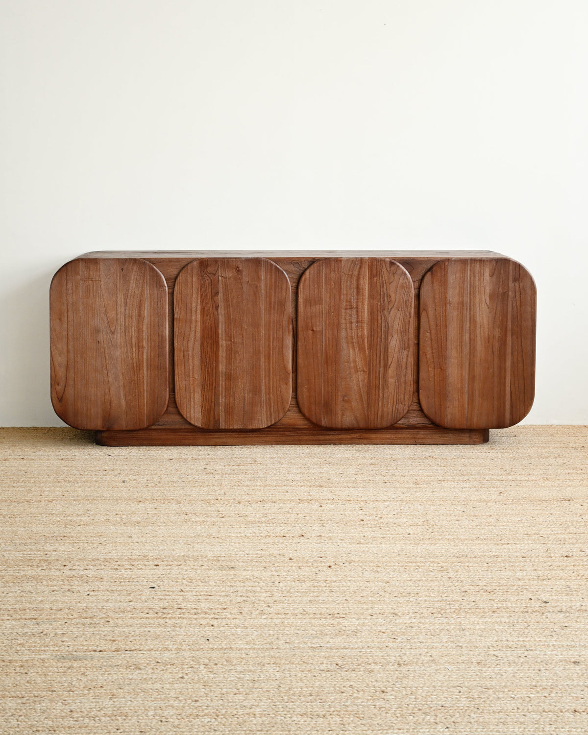 A mid-century modern wooden credenza with rounded edges and five arched door panels, shown on a woven jute rug against a plain off-white wall.