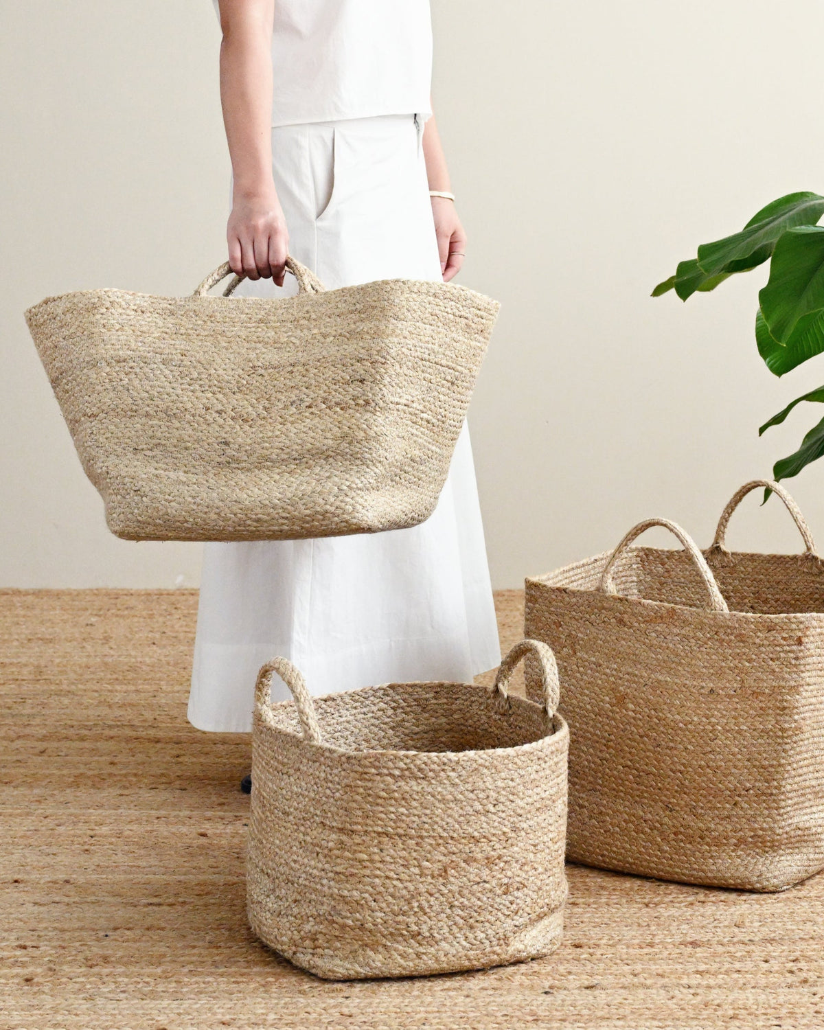 Person holding a woven basket with three other baskets on a wooden floor.