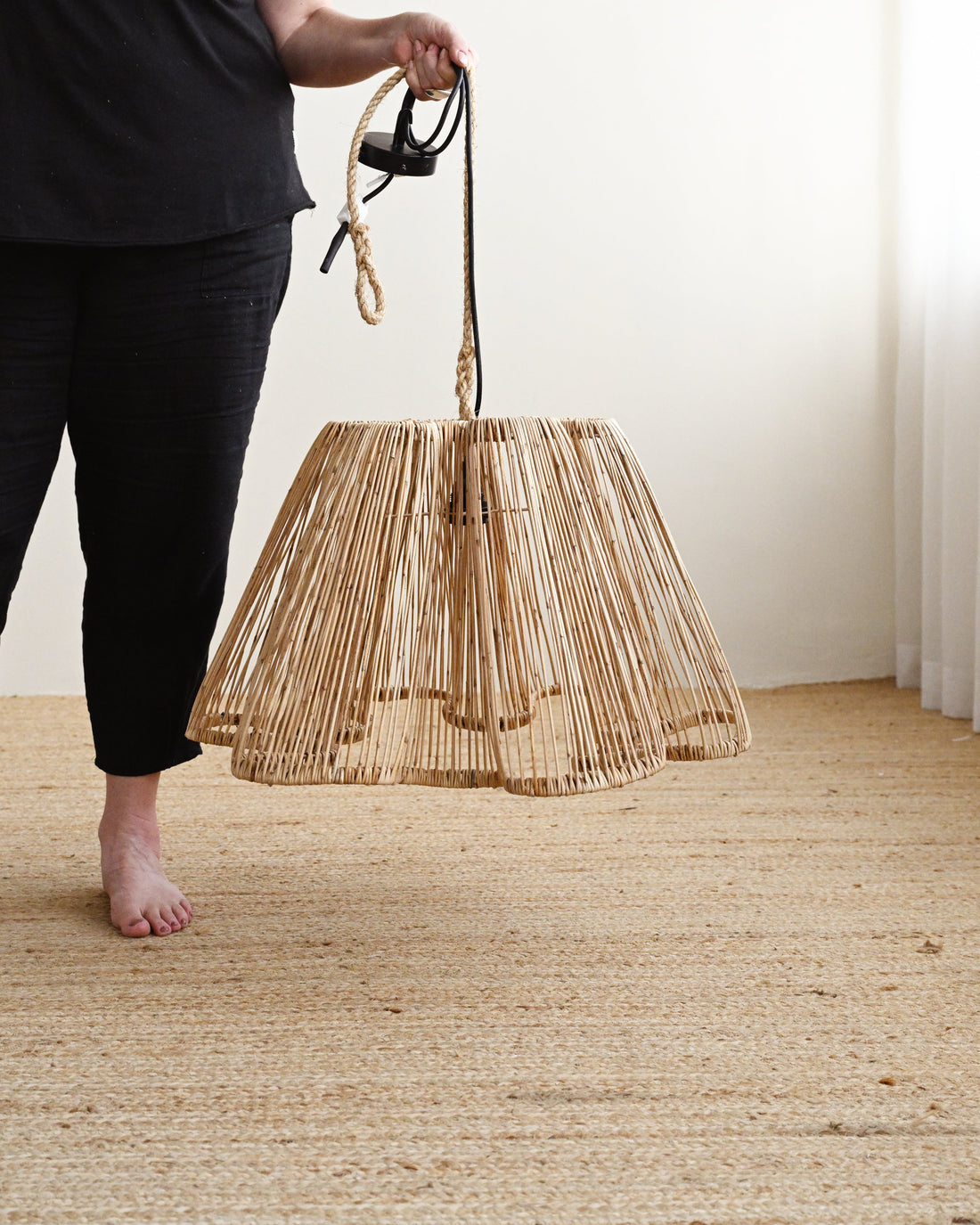 Person holding a woven bag on a wooden floor with a white wall background