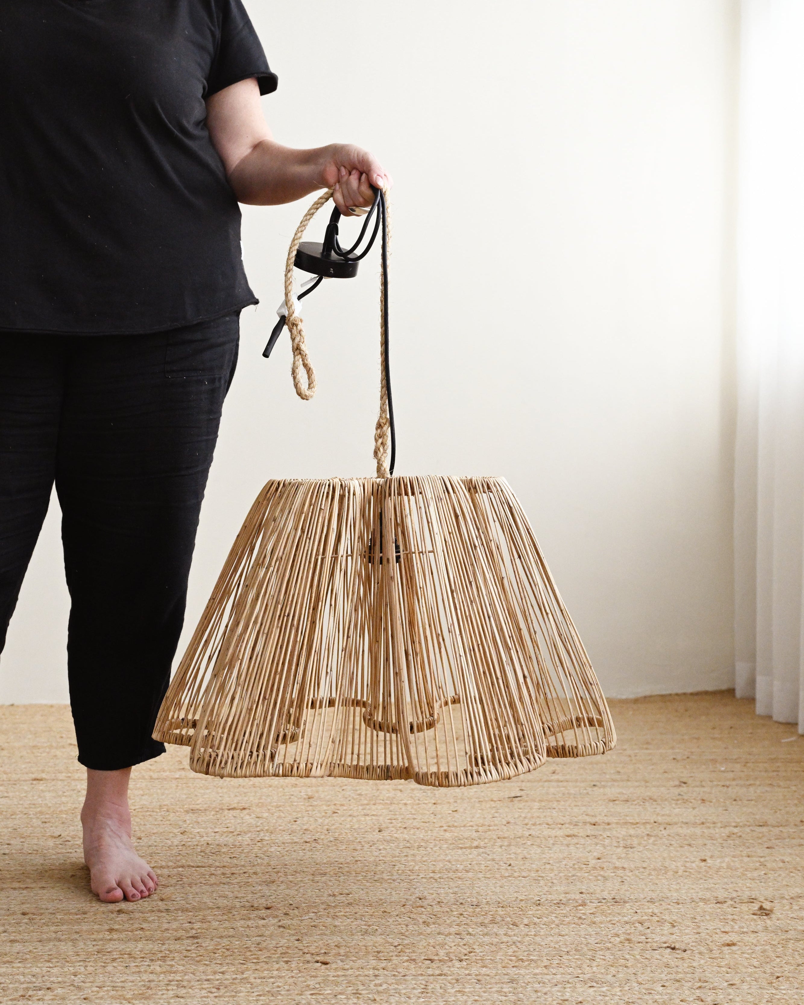 Person holding a woven bag on a wooden floor with a white wall background