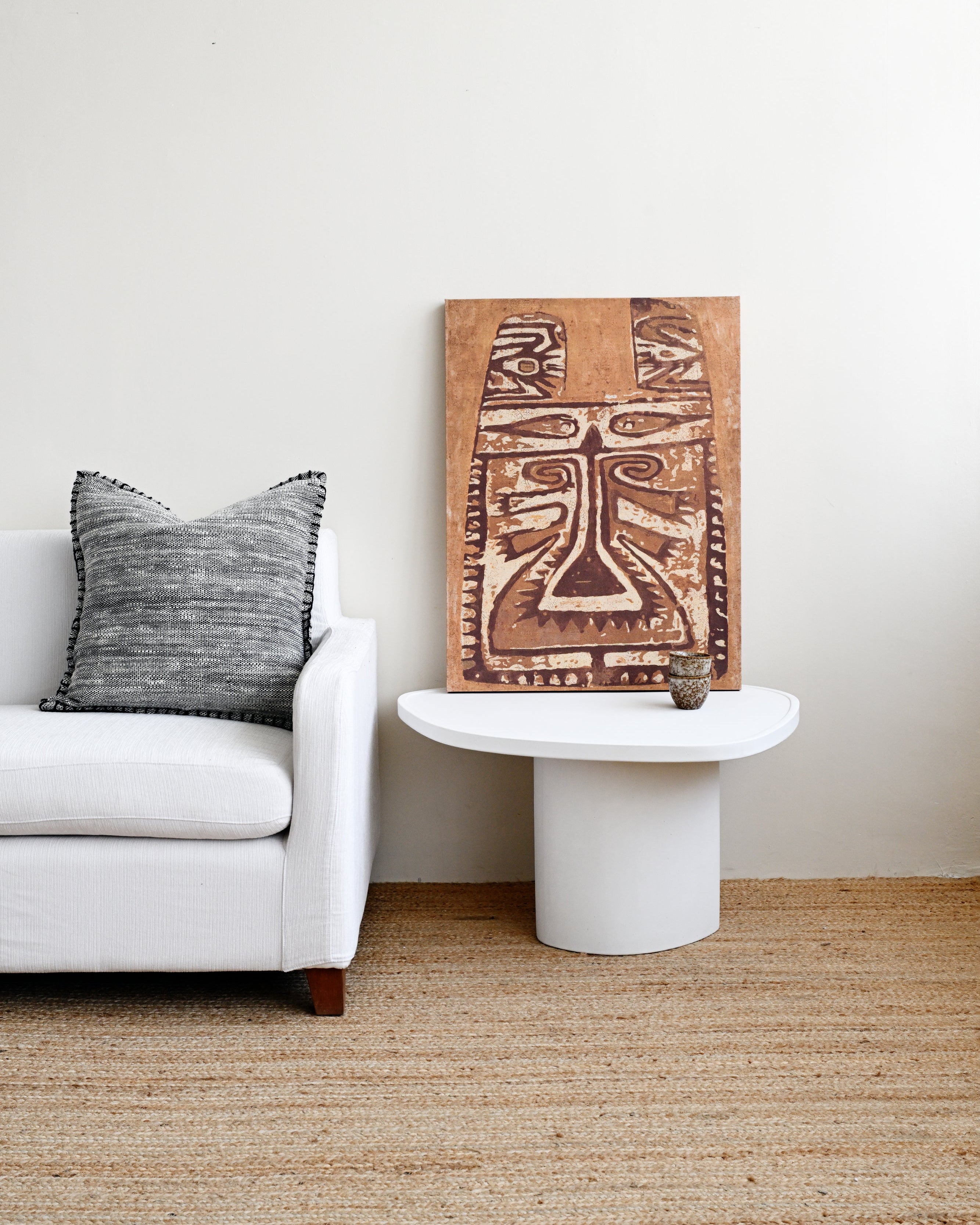 Living room with a white sofa, decorative pillow, and a wooden wall art piece.