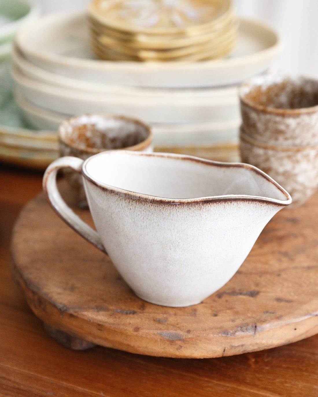 White ceramic pitcher with brown rim on a wooden surface, surrounded by other ceramic items.